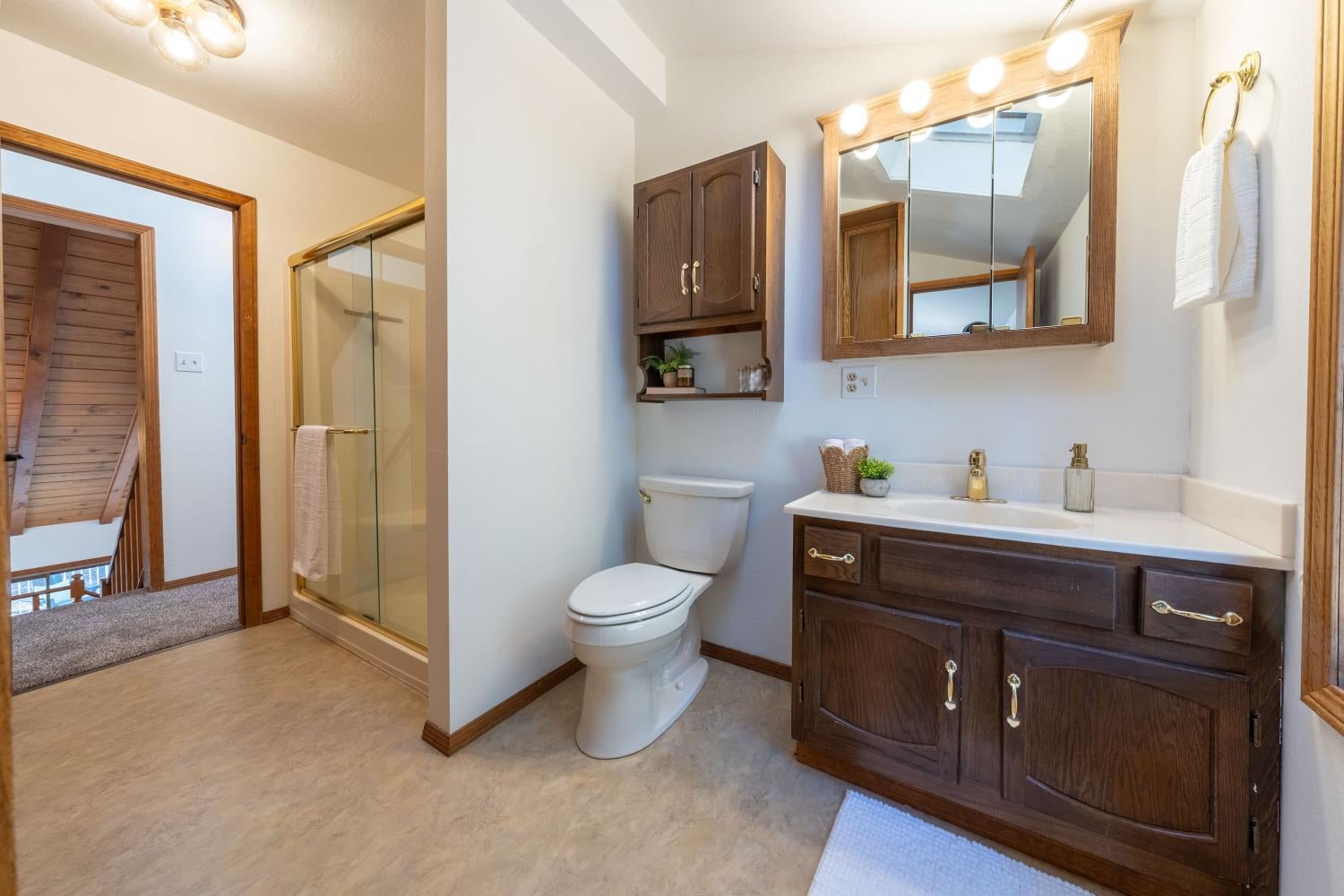 Bathroom with a dark wood vanity, glass shower, and skylight reflected in the mirror.