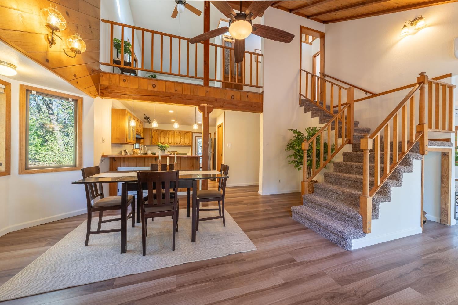 Dining area with a dark table beneath a wood-beamed ceiling, open to the kitchen and carpeted staircase.
