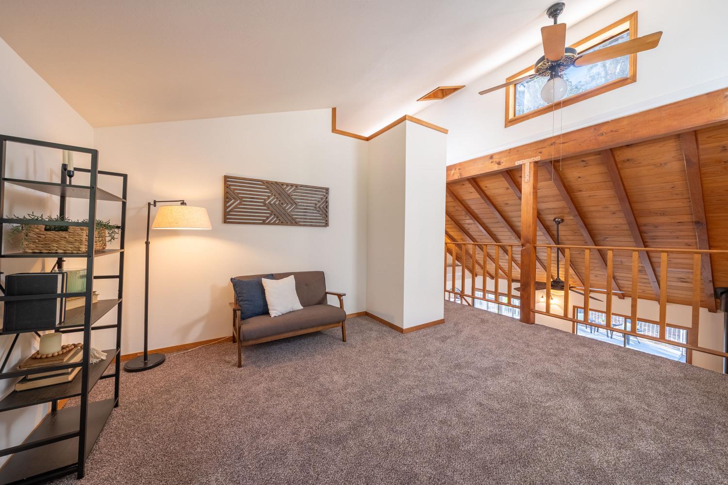 Carpeted loft sitting area with a gray loveseat, wood-beamed ceiling, and railing overlooking the lower level.