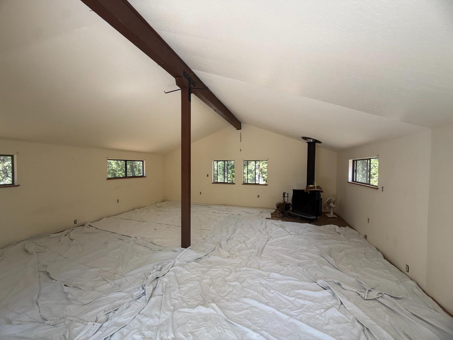 Empty vaulted room with exposed beam, wood stove, and protective sheeting covering the floor.