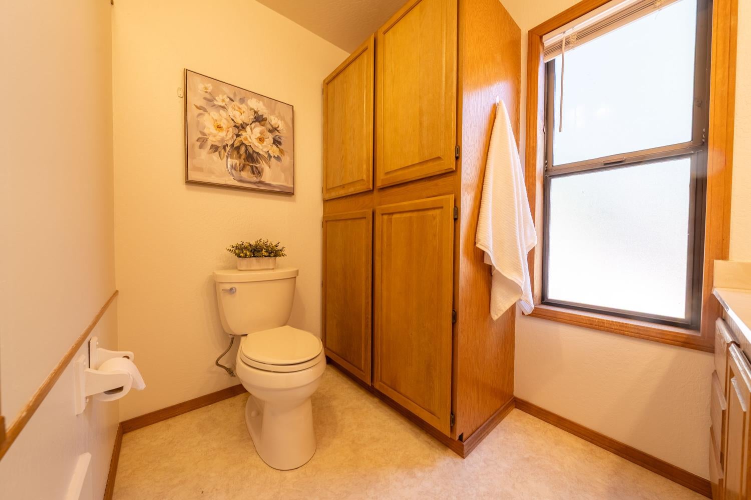 Bathroom with honey-toned wooden cabinets, a toilet, and a large window.