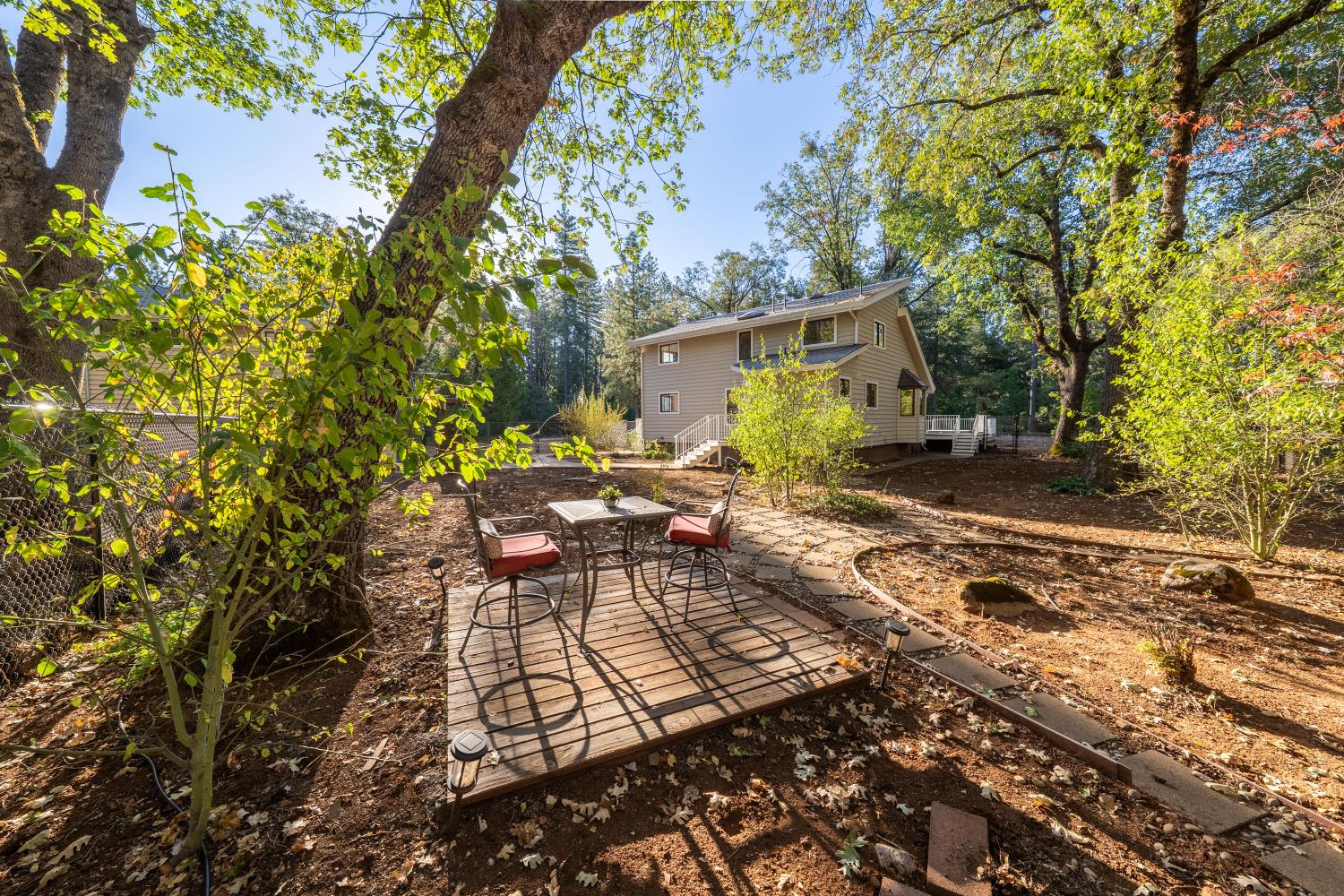Wooded backyard with a tan two-story house, raised deck, and outdoor table and chairs.