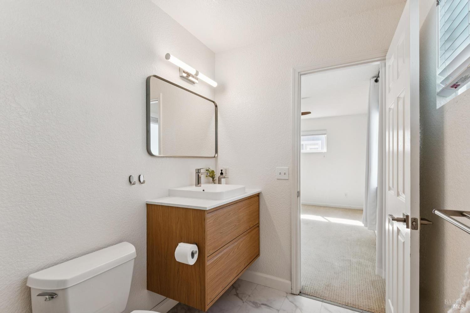Bathroom with a wood-front vanity and white vessel sink beside an open doorway to a carpeted room.