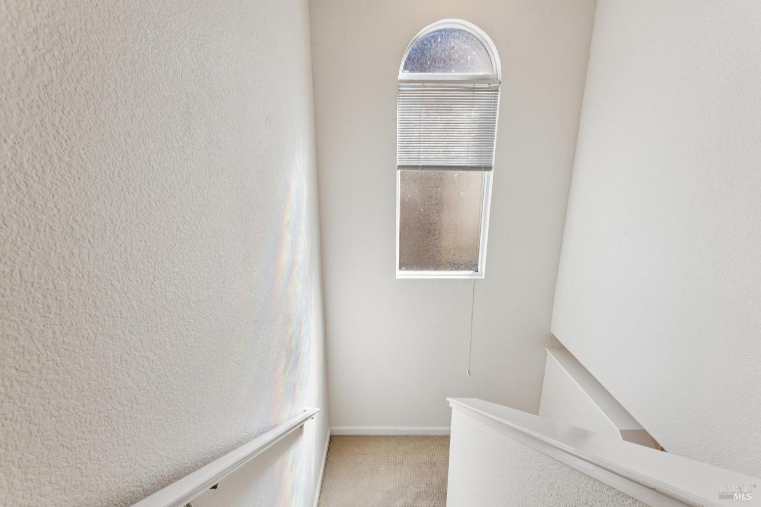 Empty stairwell with carpeted steps and a tall arched window with blinds.
