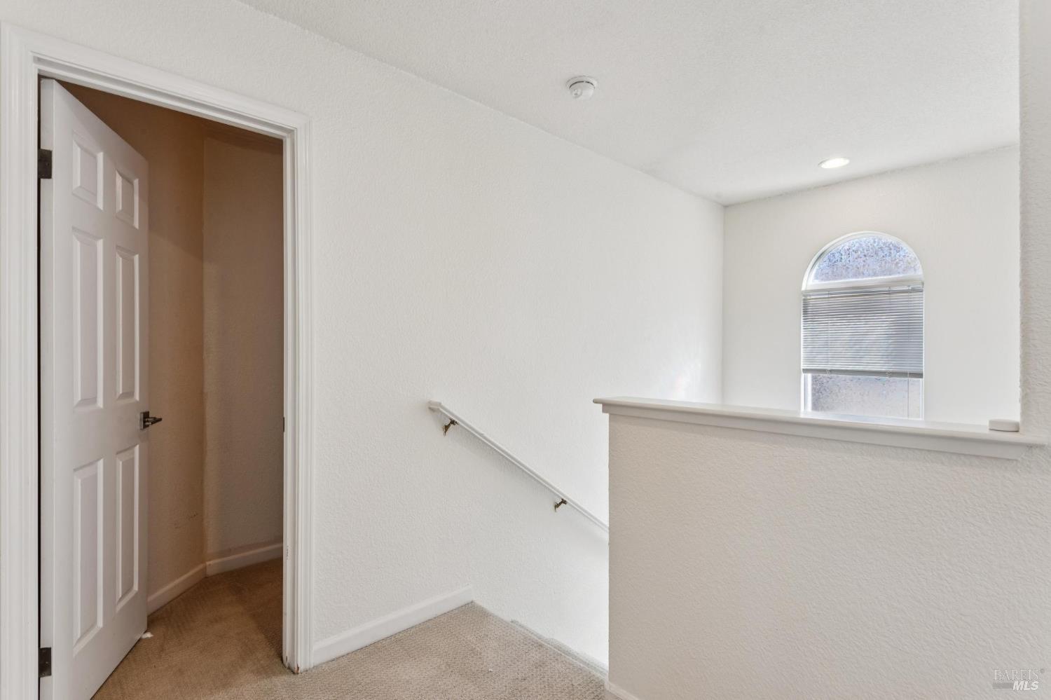 Carpeted upstairs landing with a stair railing, open doorway, and arched window.