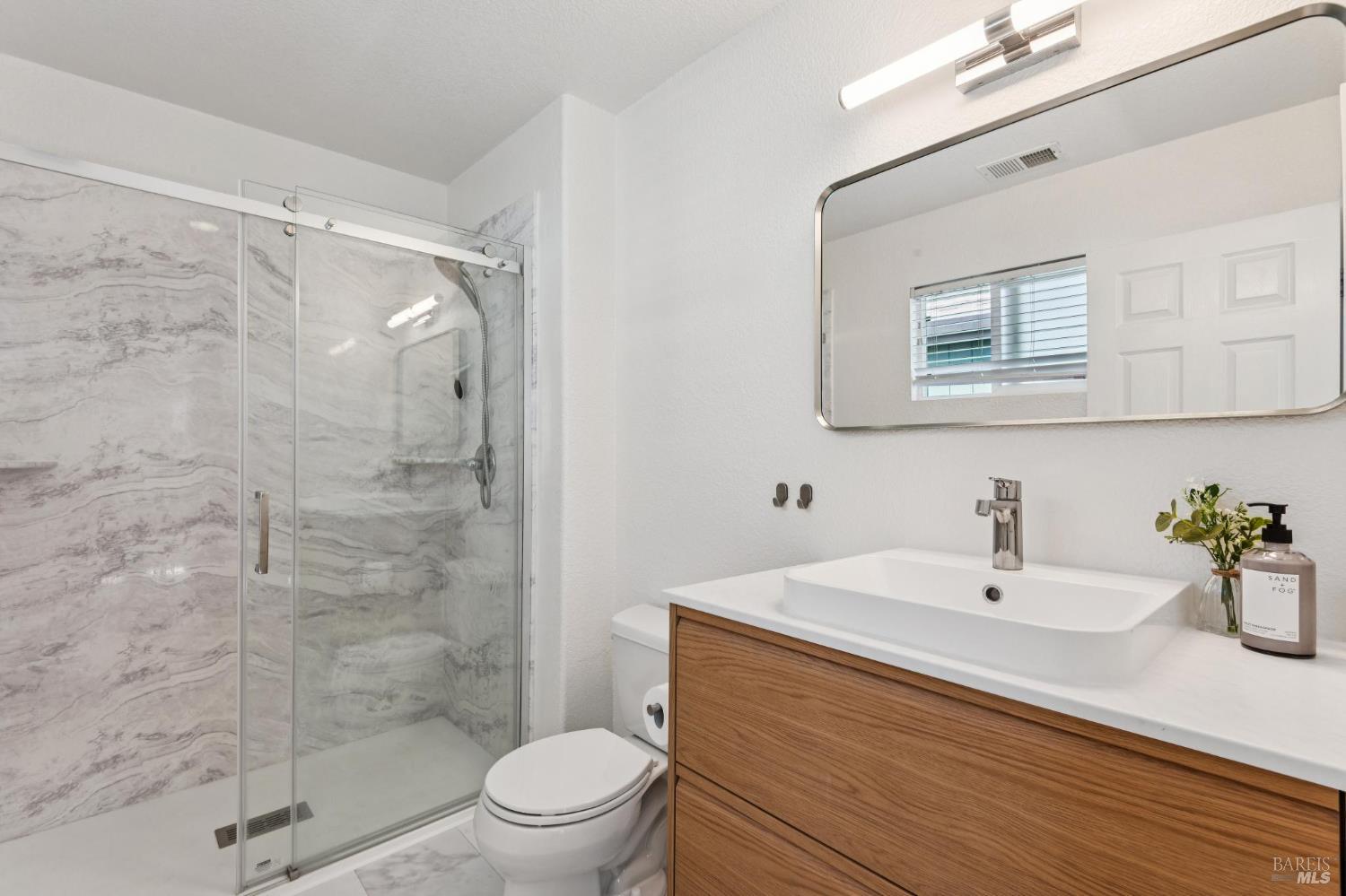 Bathroom with a marble-look tiled shower and a wood-front vanity.