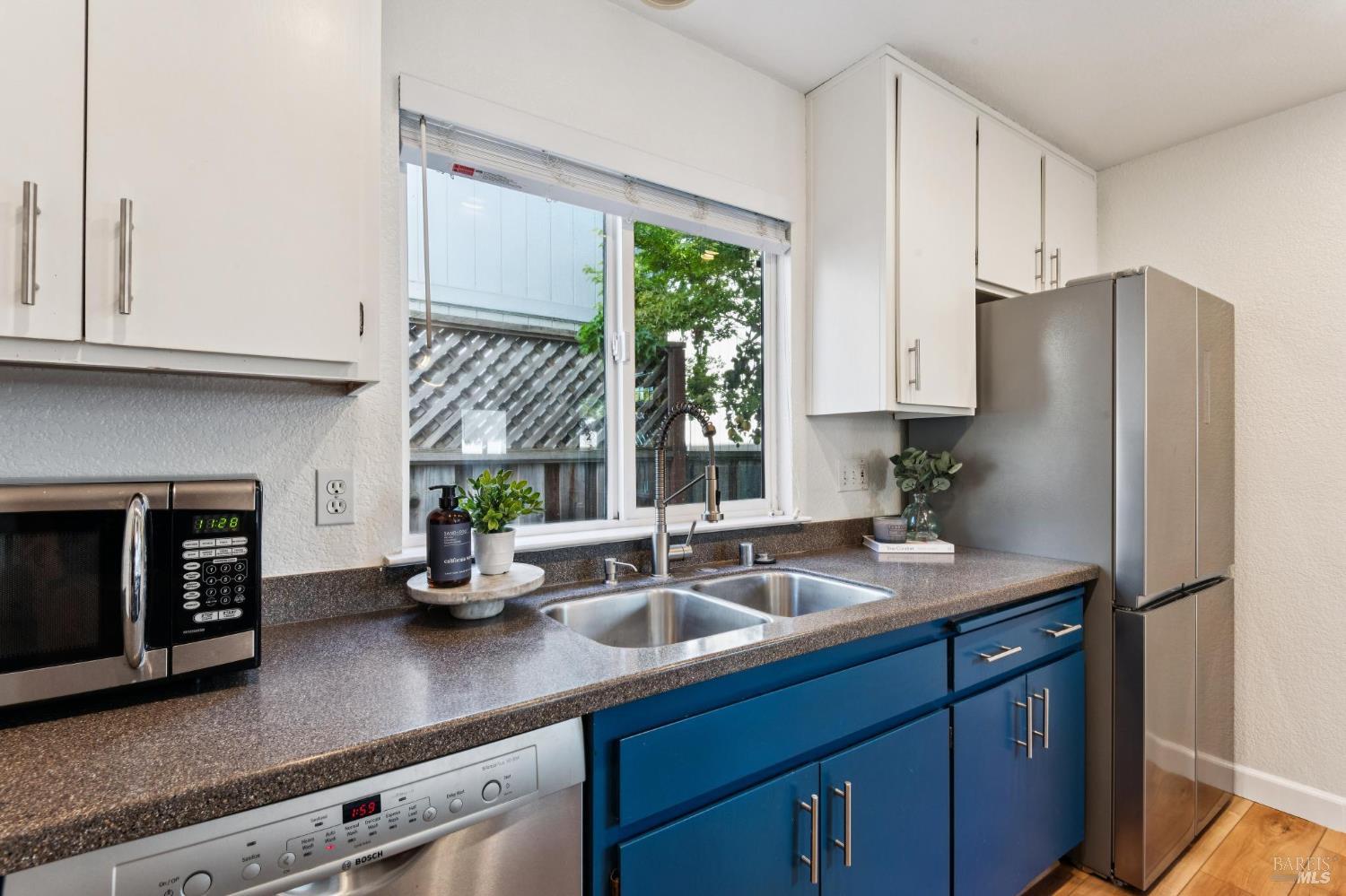 Kitchen with blue cabinets, a double-basin sink beneath a window, and stainless steel appliances.