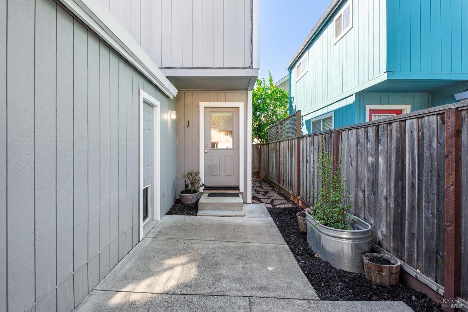 Side entrance with a concrete walkway, wooden privacy fence, and raised planters.