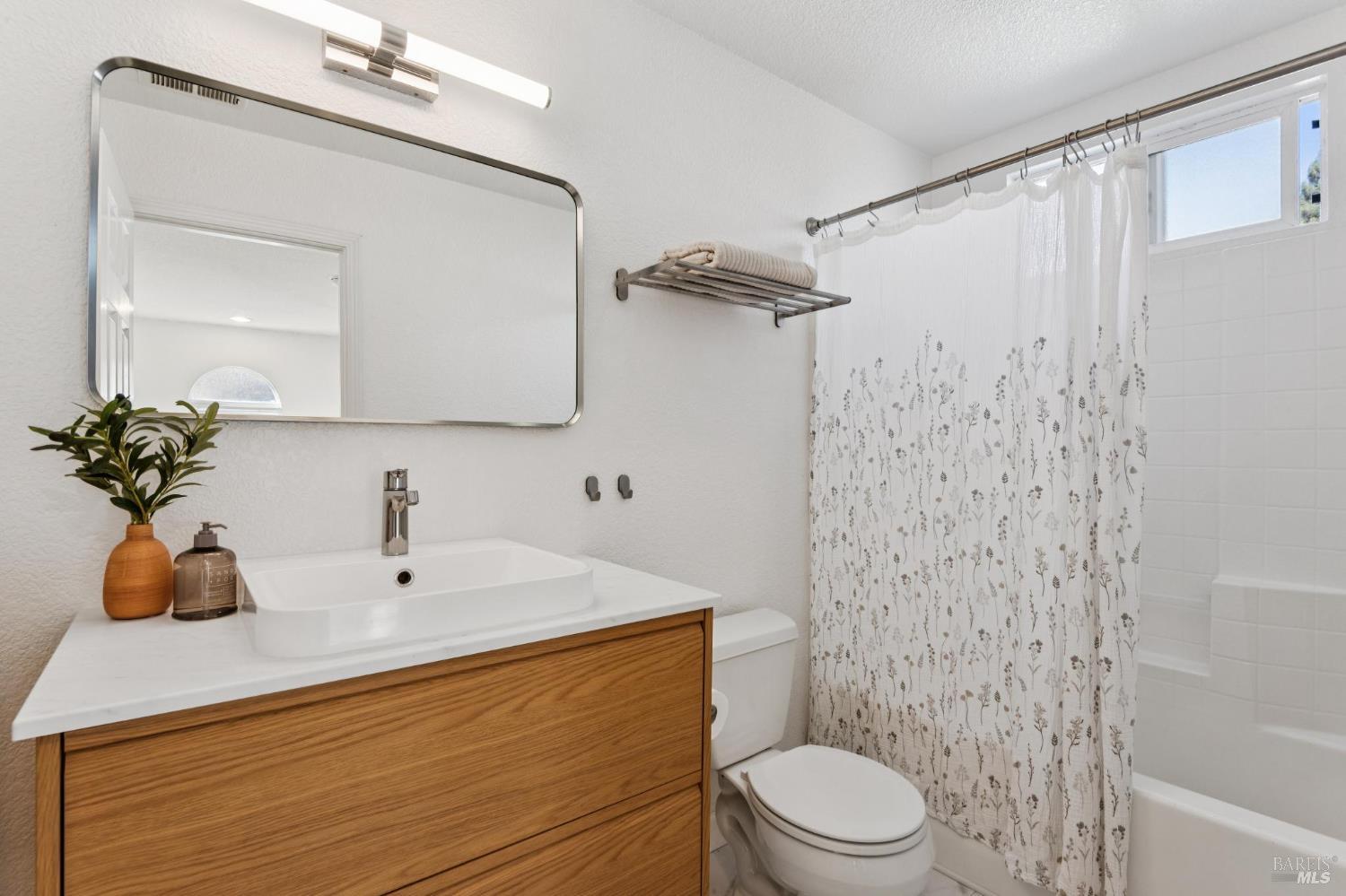 Bathroom with a wood vanity, vessel sink, floral shower curtain, and bathtub.