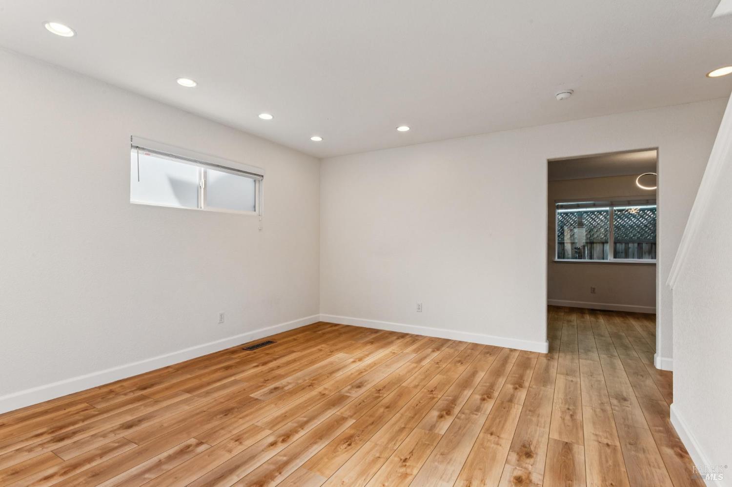 Empty room with warm wood flooring, recessed lights, and a small horizontal window.