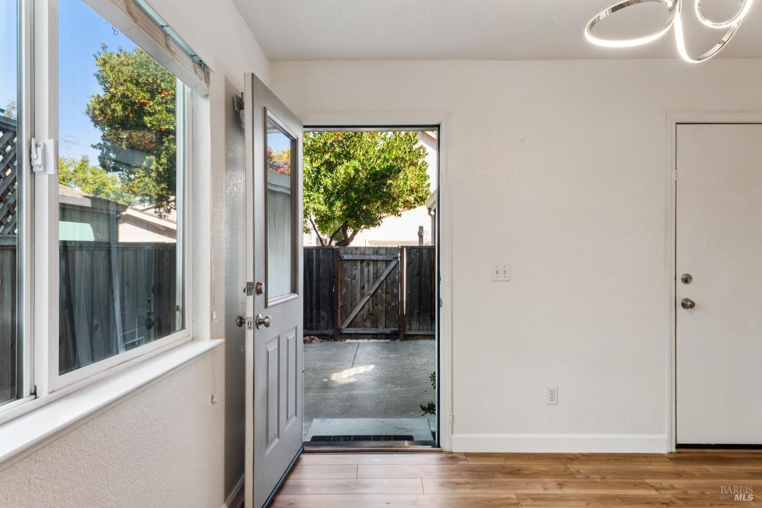 Entry area with wood-look flooring, large window, and open door to a fenced patio.