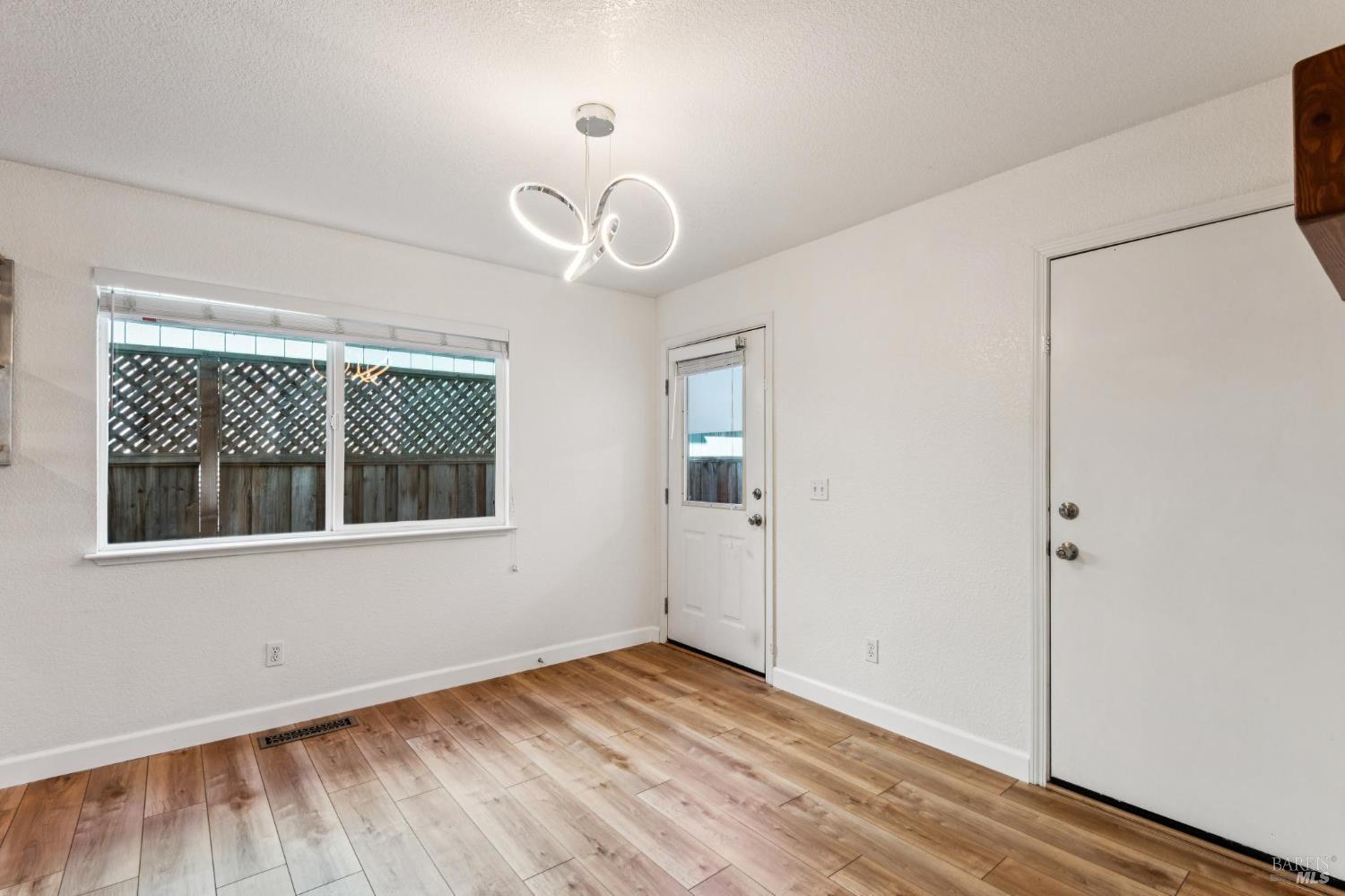 Empty room with wood-look flooring, a large window, two white doors, and a looping ceiling light.