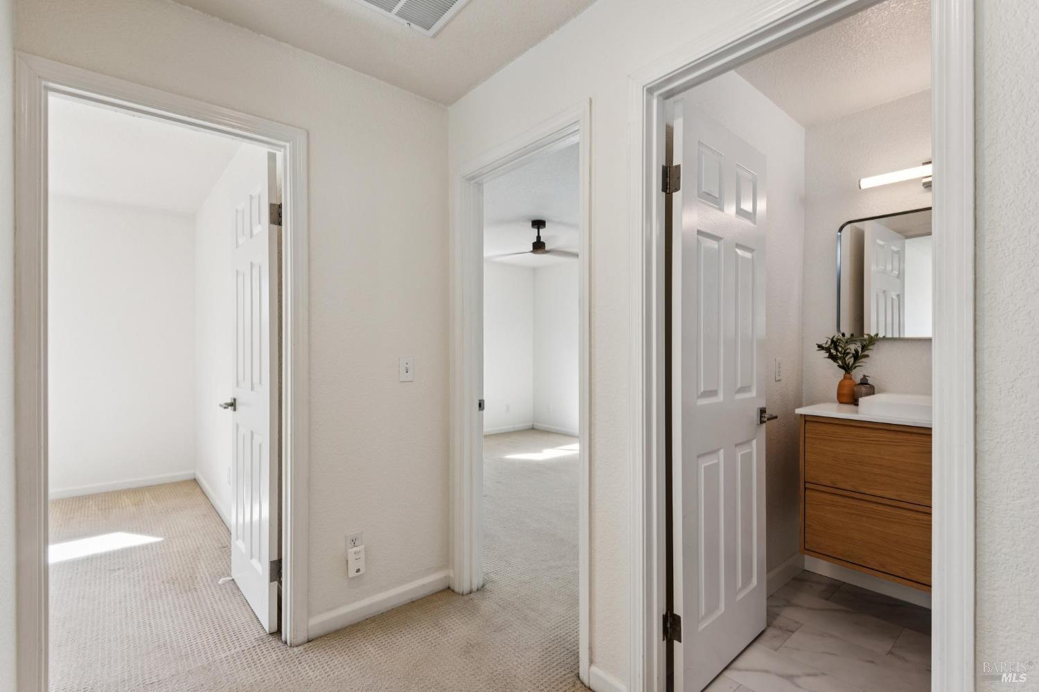 Hallway with open doorways to a carpeted bedroom and a bathroom with a wood vanity.