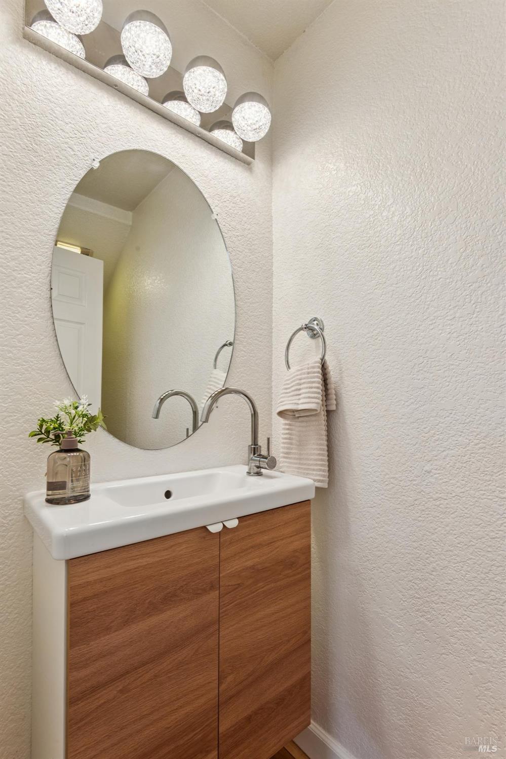 Bathroom vanity with a wood cabinet, oval mirror, and globe lights.