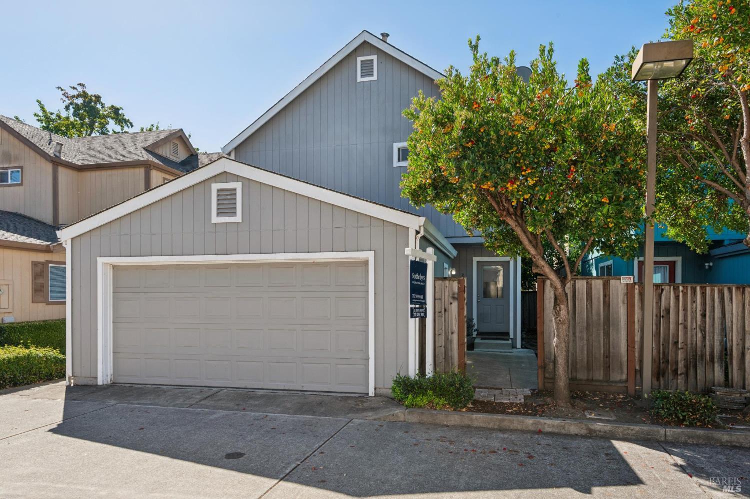 Gray two-story home with a large garage, fenced entry, and leafy tree.
