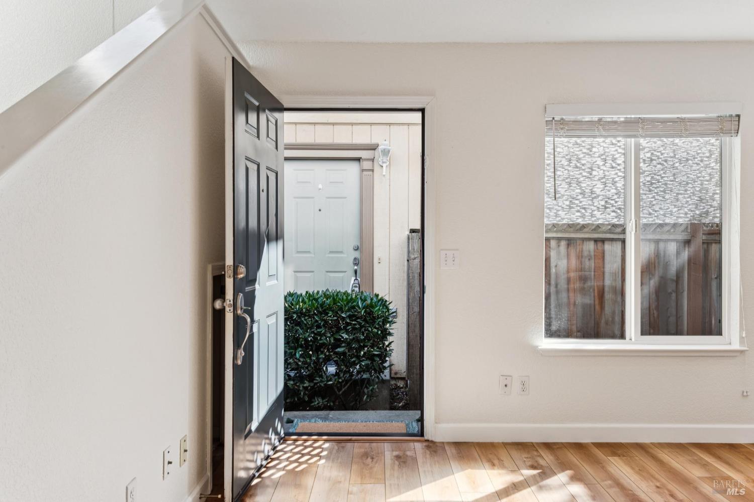 Entryway with an open dark front door, light wood flooring, and a window with blinds.