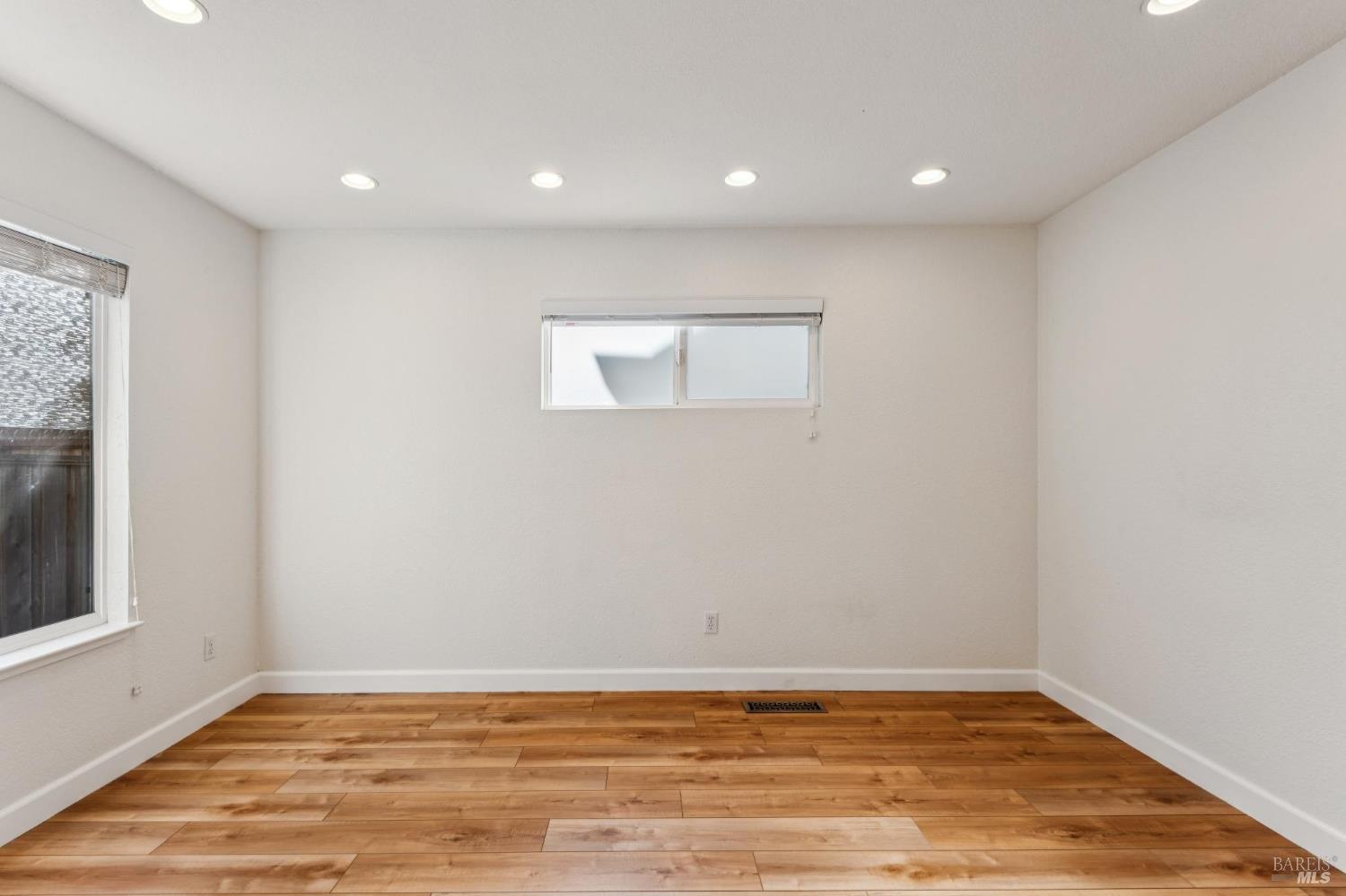 Empty room with wood-look plank flooring, recessed lights, and two windows.