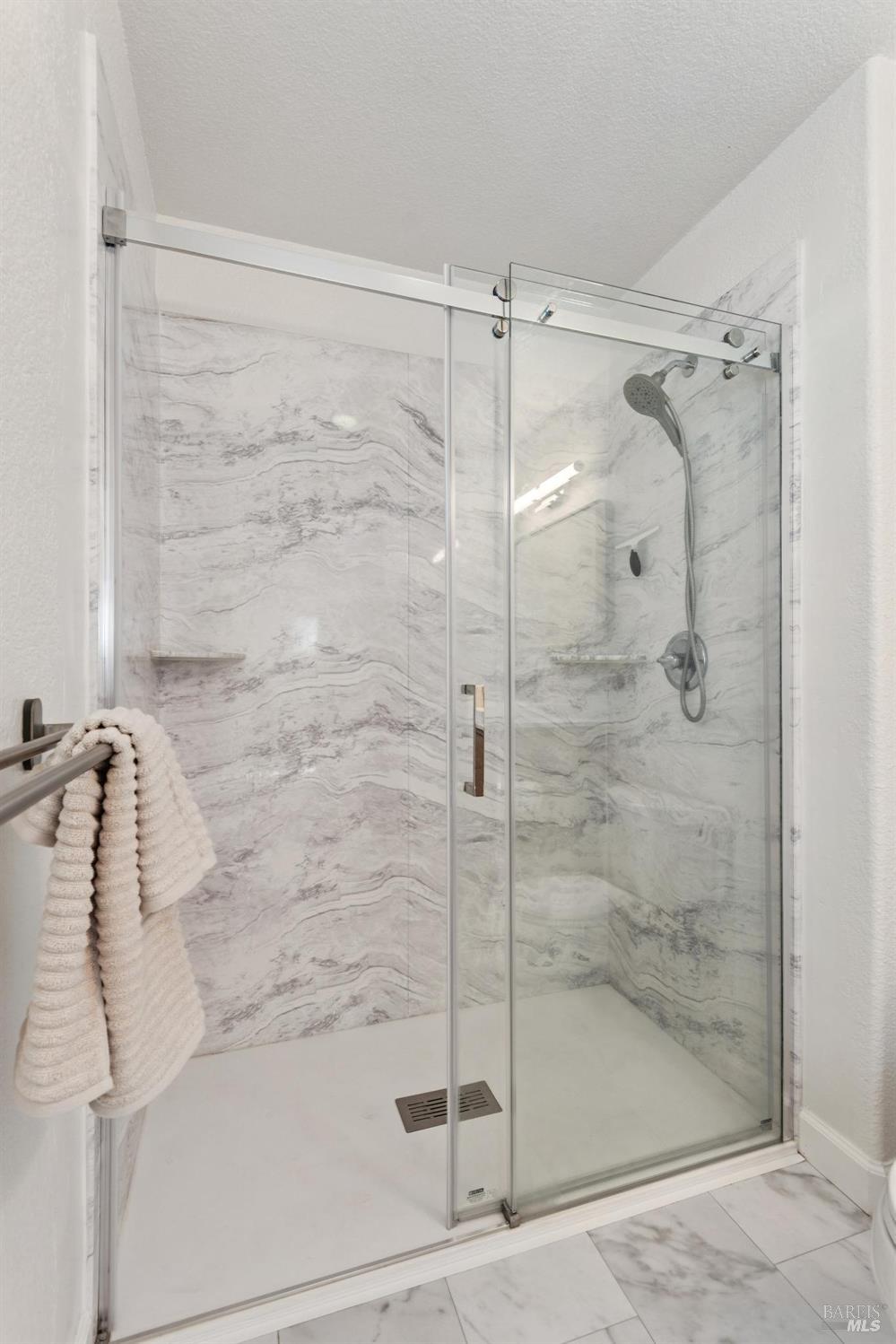 Bathroom shower with sliding glass doors, gray-veined tile, and a handheld showerhead.