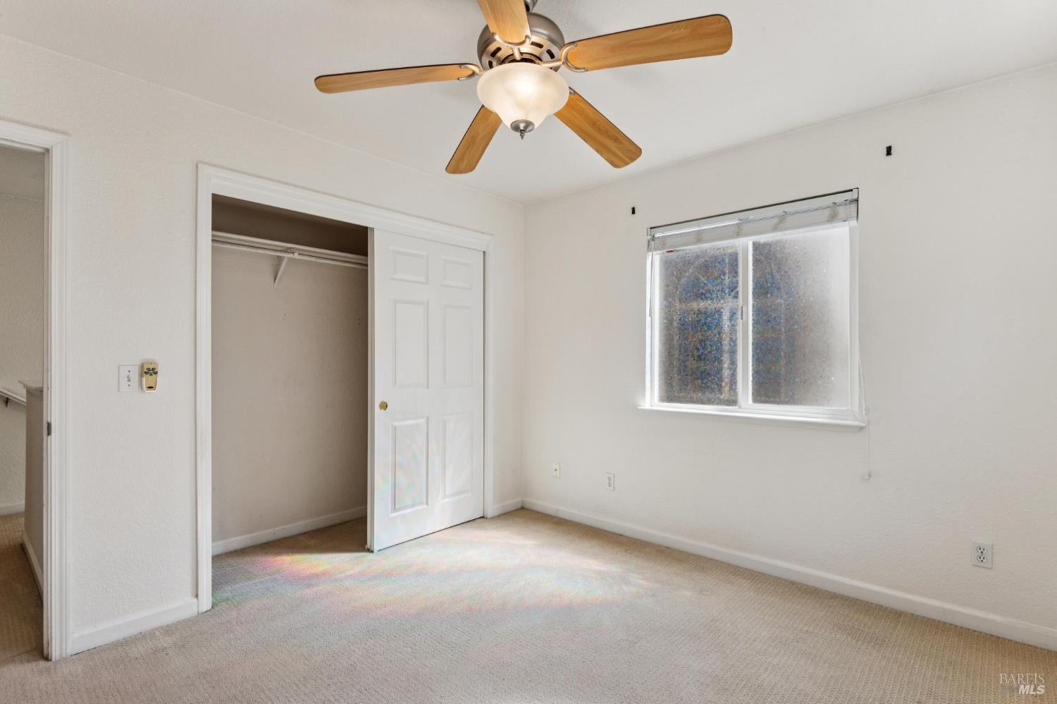 Empty bedroom with a wood-blade ceiling fan, carpet, and an open closet.
