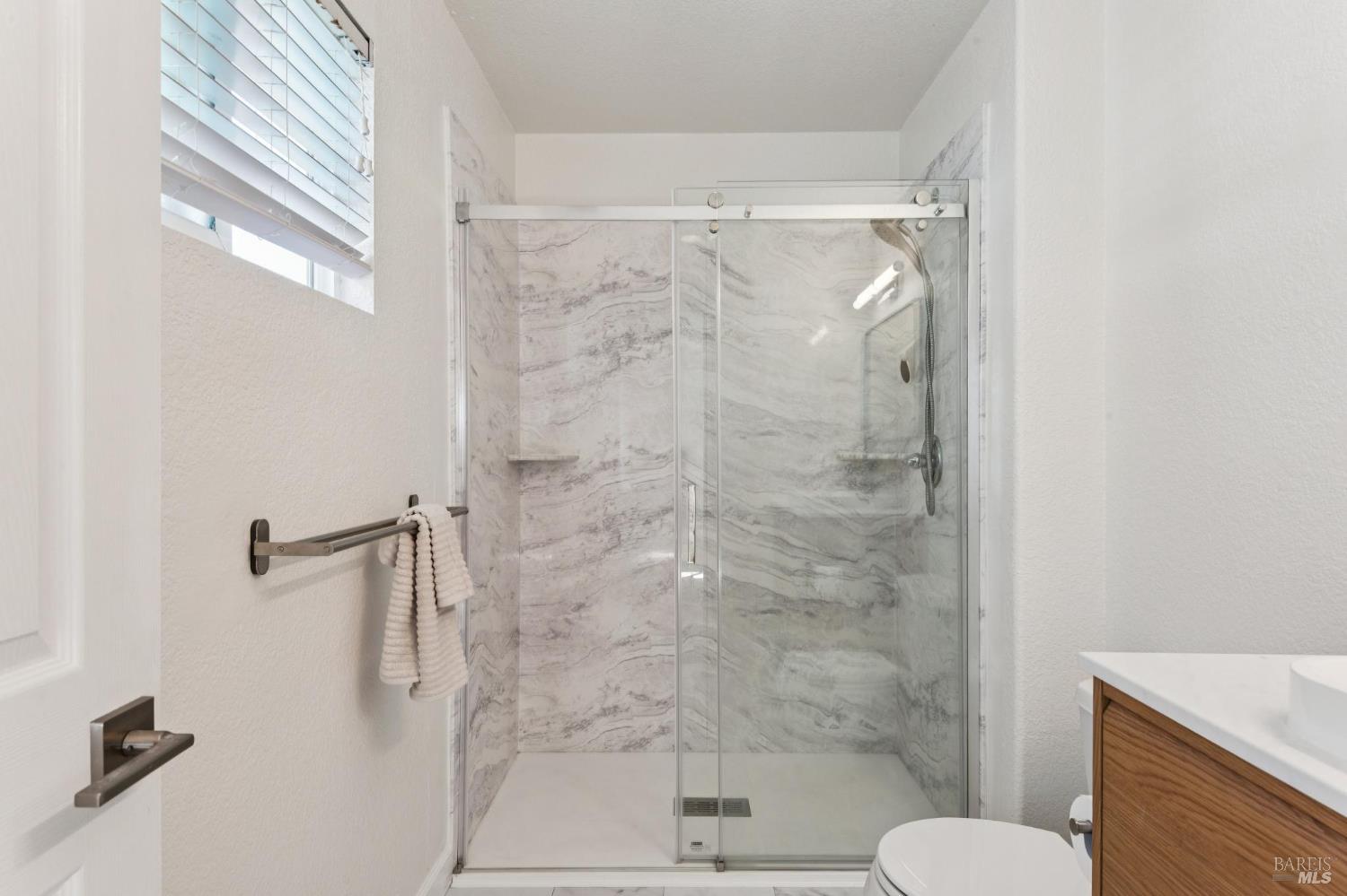 Bathroom with a glass-enclosed shower featuring gray-veined tile and a handheld showerhead.