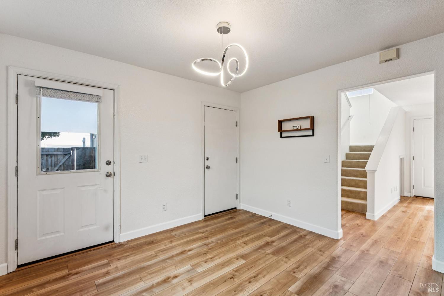 Entryway with wood-look flooring, a loop pendant light, and a carpeted staircase.