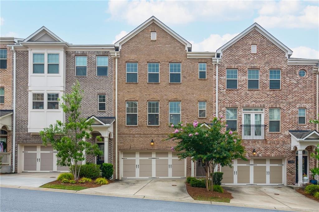 Brick townhouse with a double garage, white-trimmed windows, and landscaped trees.