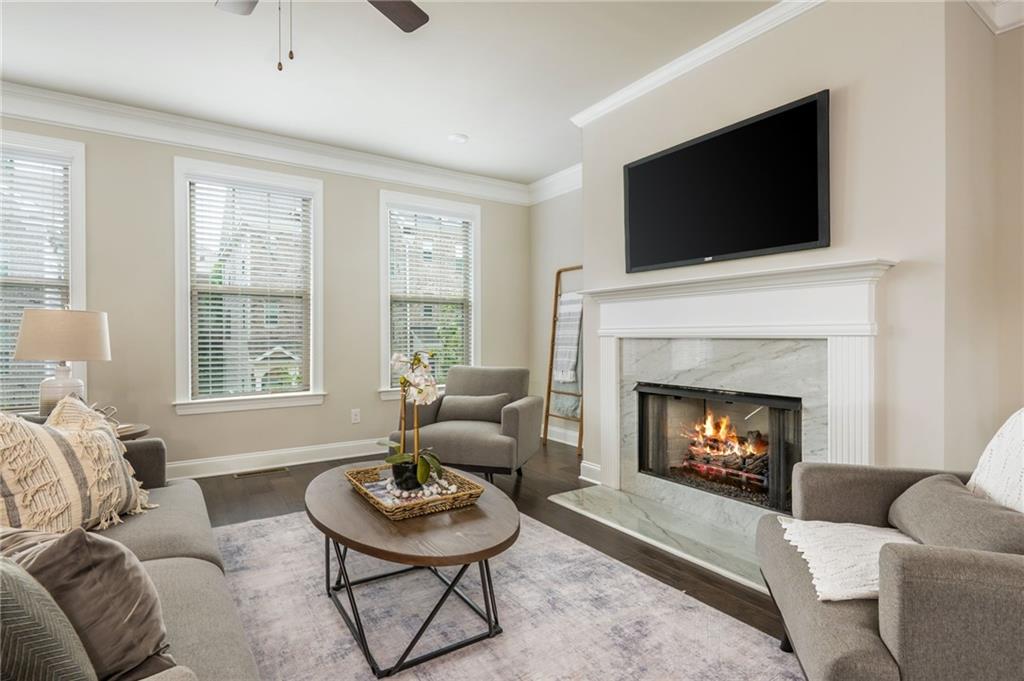 Furnished living room with a marble fireplace, lit fire, and tall windows.