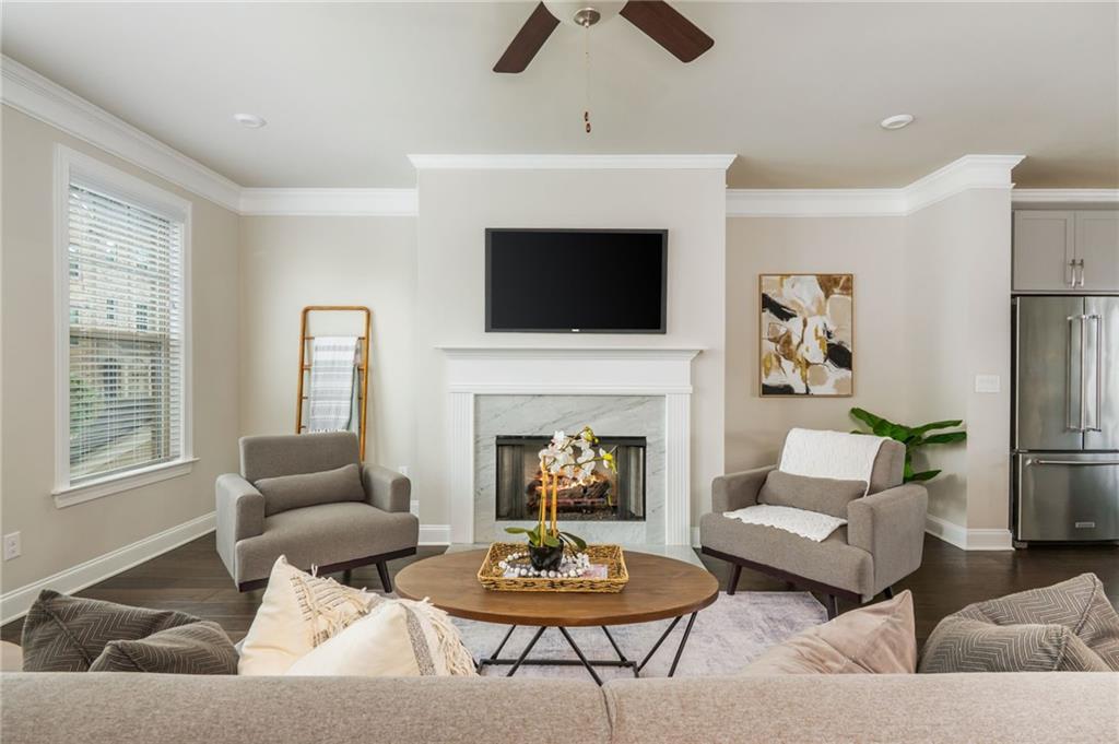 Staged living room with a white fireplace, mounted television, gray armchairs, and round wood coffee table.