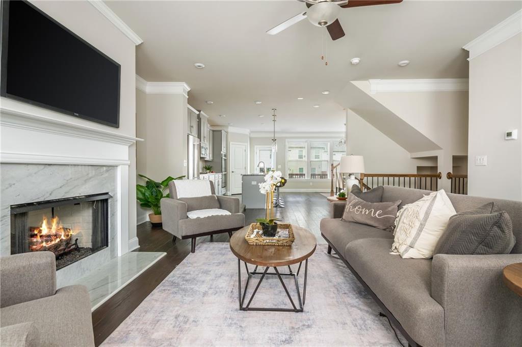 Open-plan living room with a gray sectional, marble-surround fireplace, and kitchen beyond.