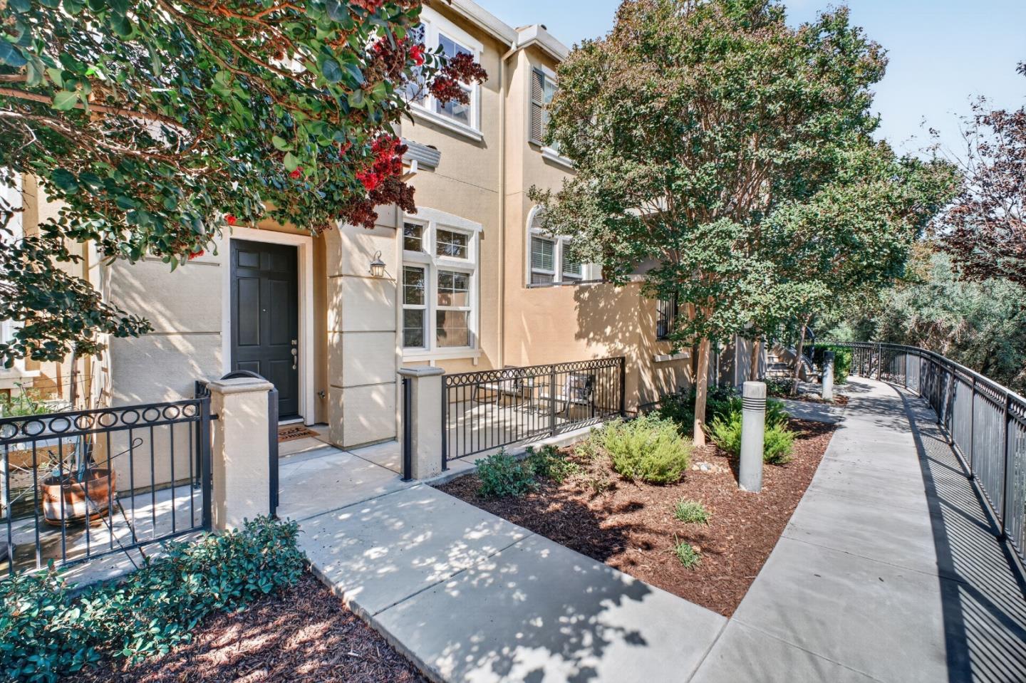 Beige building entrance beside a landscaped walkway with black metal railings and mature trees.
