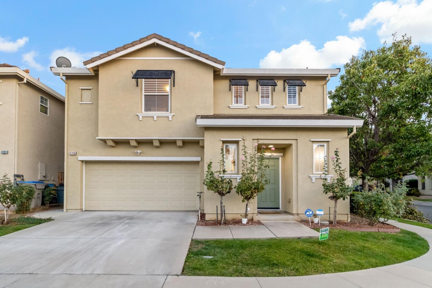 Two-story beige stucco house with an attached double garage, covered entry, and landscaped front lawn.