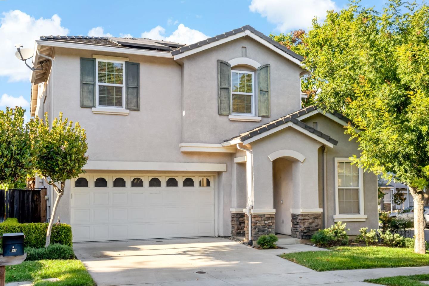 Two-story stucco home with a double garage, dark shutters, and stone accents.