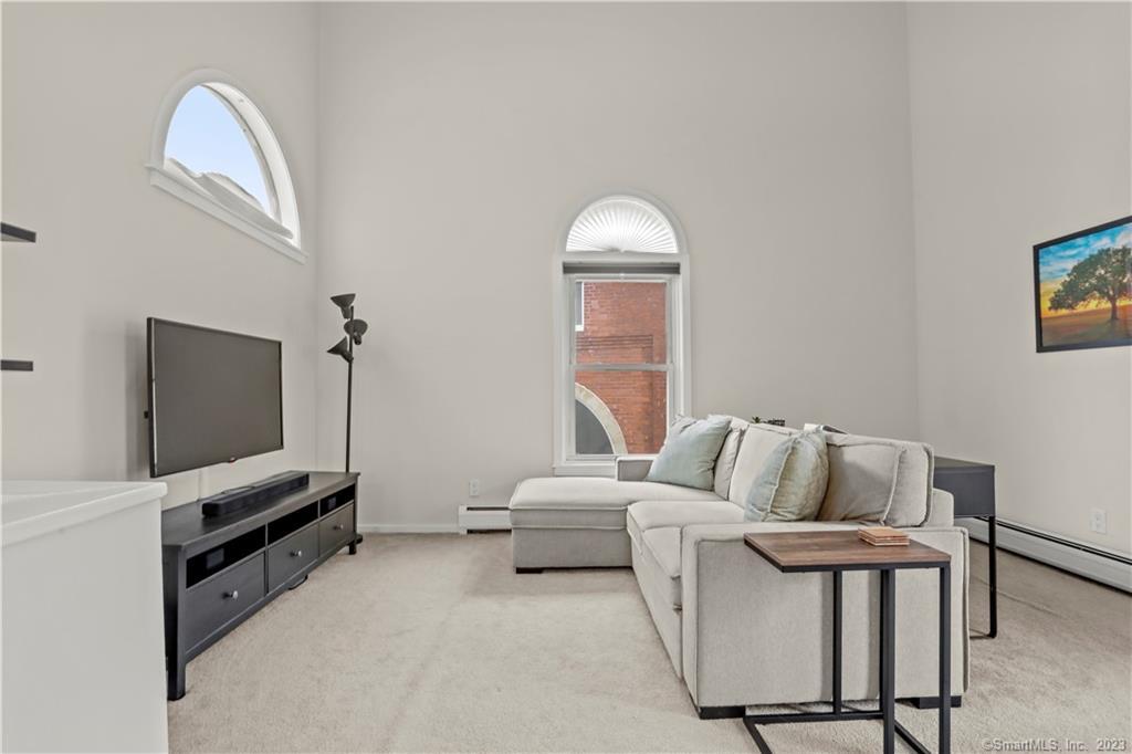 Living room with a light sectional sofa, carpet, and two arched windows beneath a high ceiling.