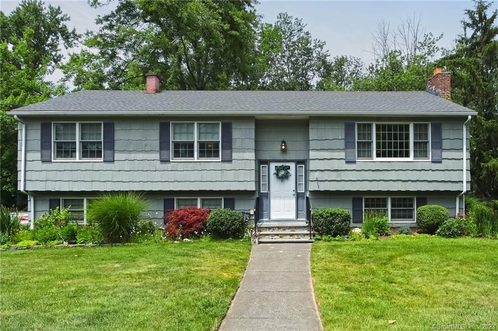 Gray split-level home with dark shutters, a centered white door, and a walkway across the lawn.