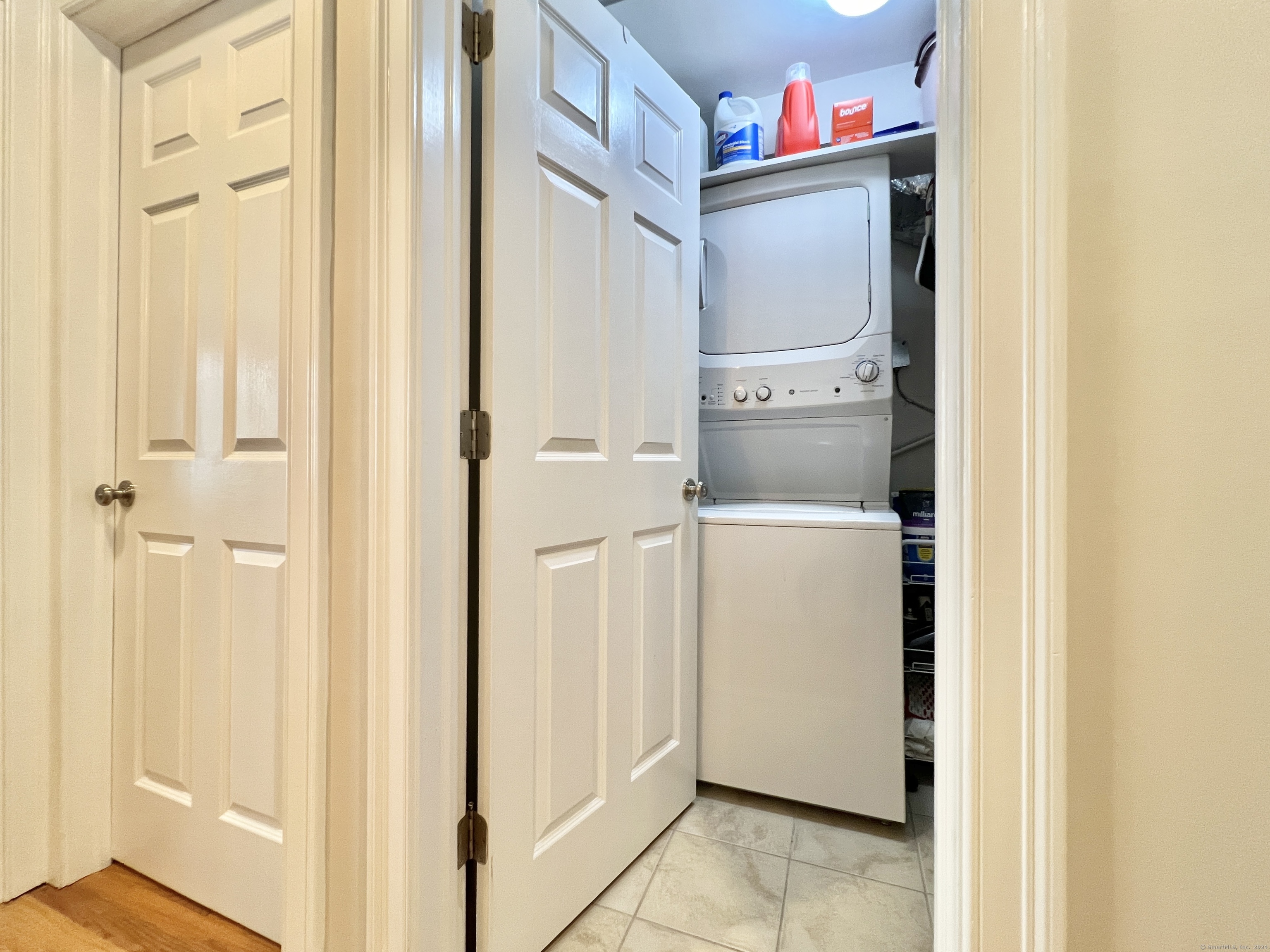 Stacked washer and dryer in a laundry closet with open doors and tiled flooring.