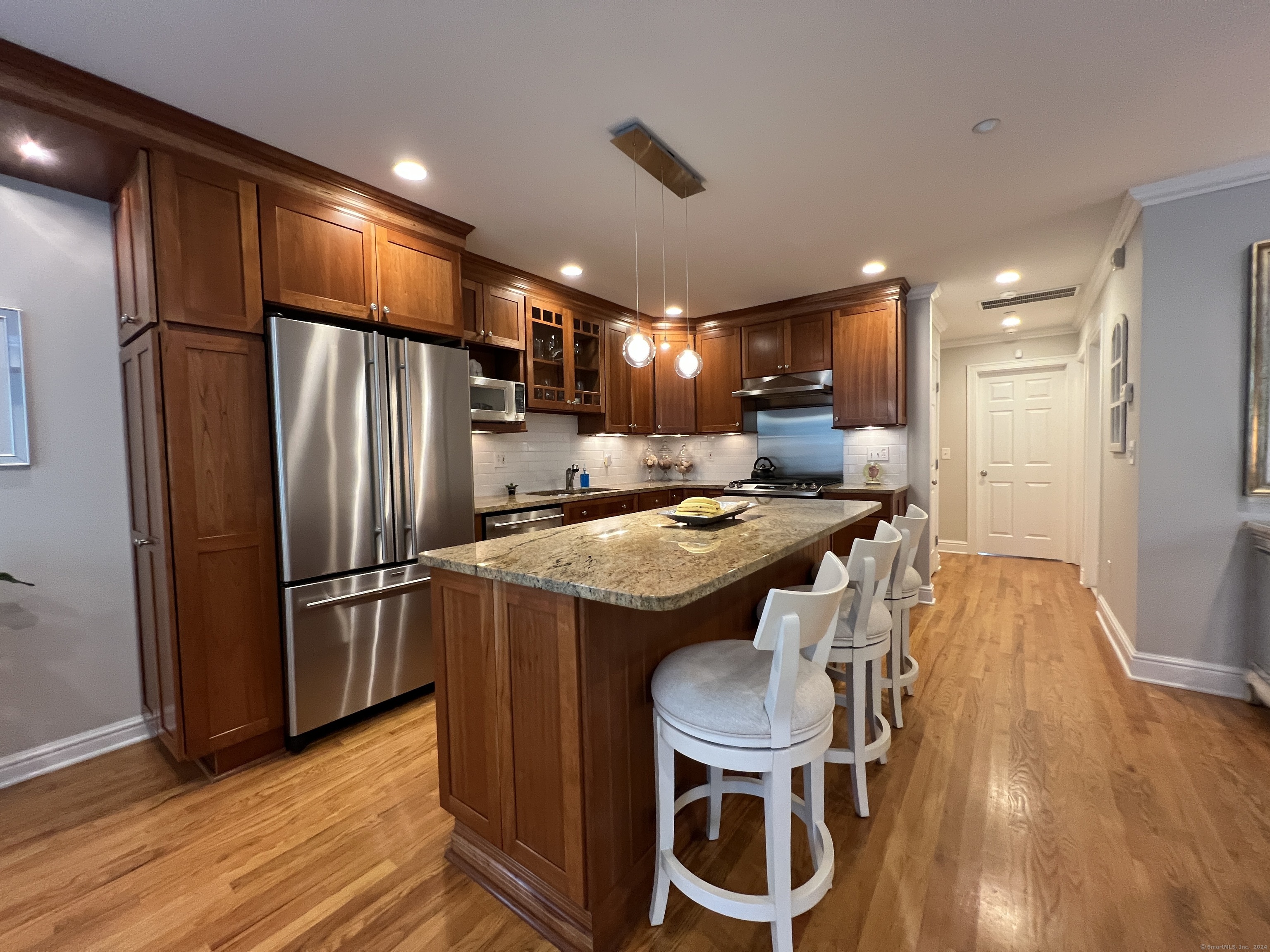 Kitchen with dark wood cabinetry, stainless steel appliances, and a large granite island with white stools.