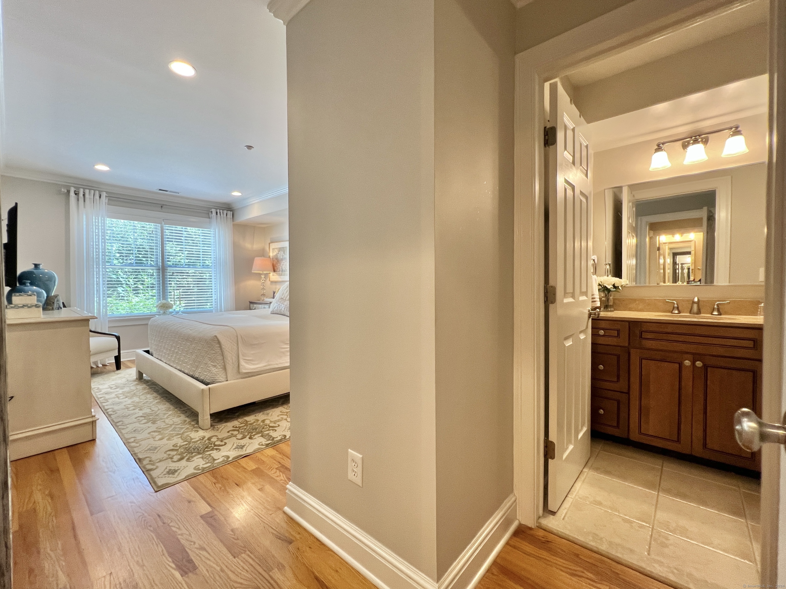 Bedroom and adjoining bathroom, with a large window, hardwood floors, and a dark wood vanity.