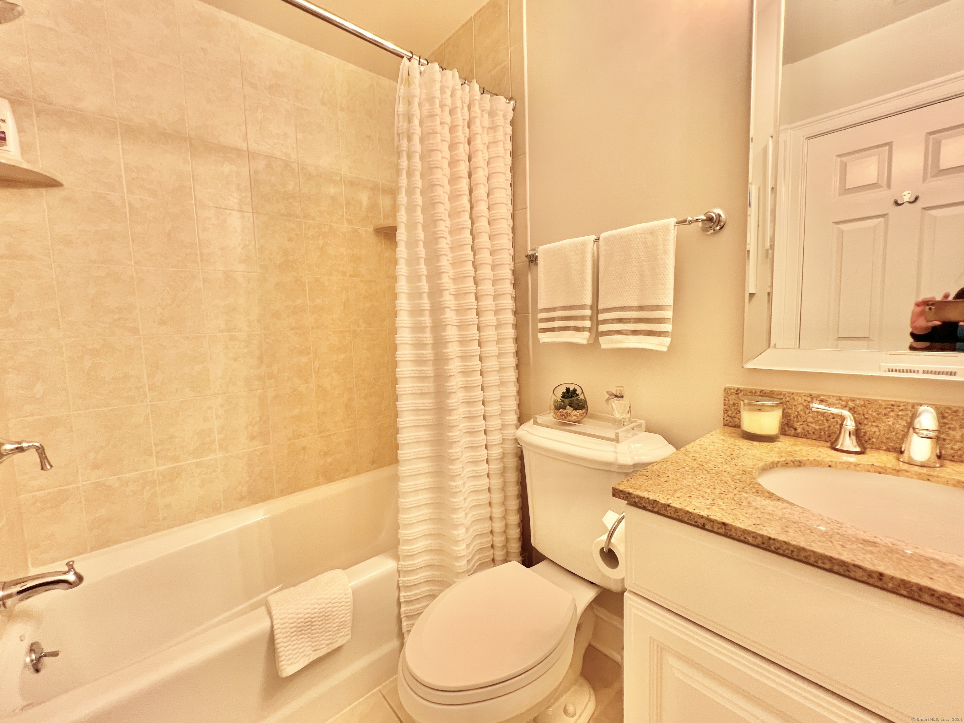 Bathroom with beige tiled tub surround, white shower curtain, and granite-topped vanity.