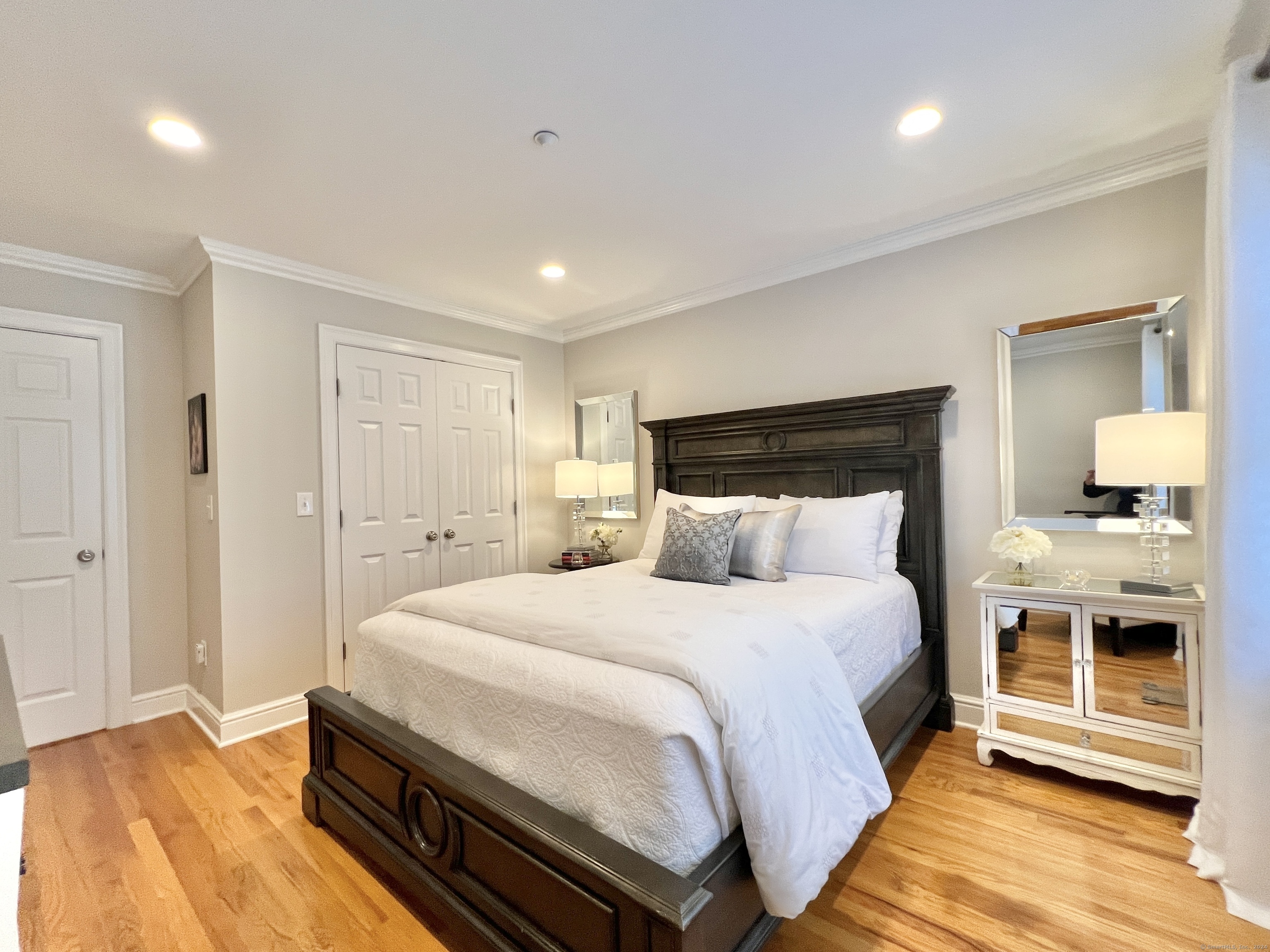 Furnished bedroom with a dark wood bed, white bedding, and warm hardwood floors.