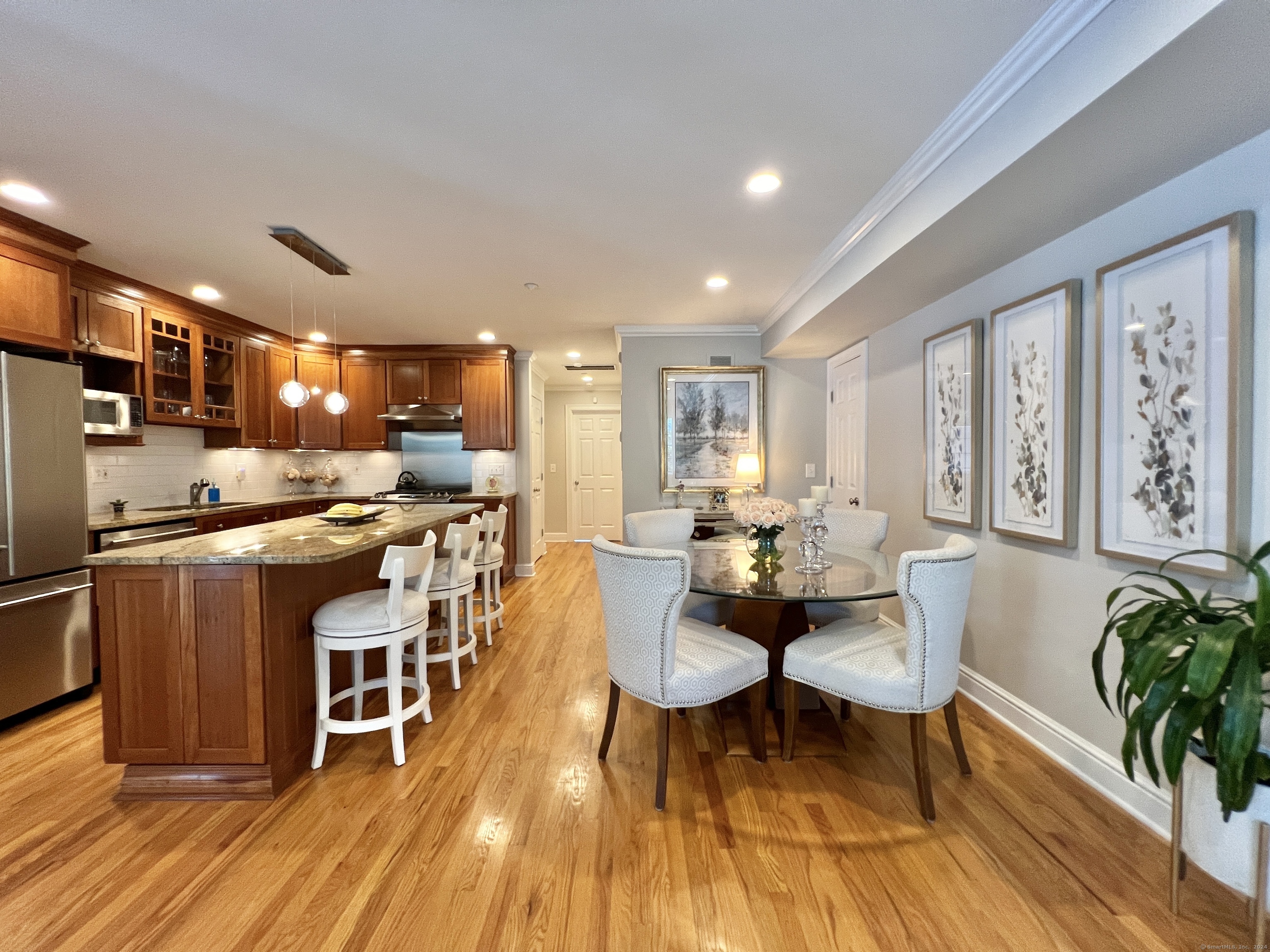 Open kitchen and dining area with cherry cabinets, granite island, hardwood floors, and upholstered dining chairs.