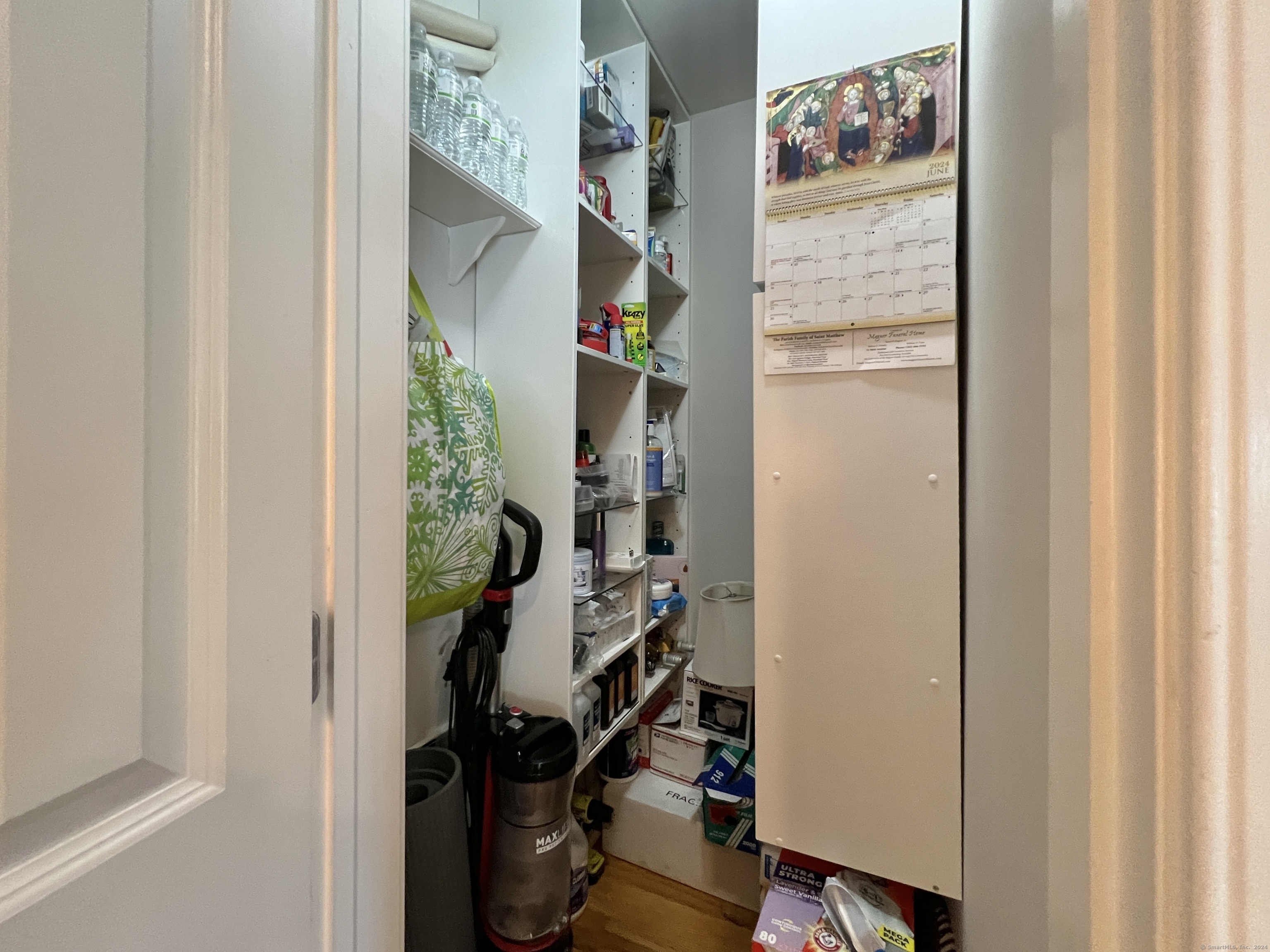Storage closet with crowded shelves of household supplies and a vacuum on the floor.