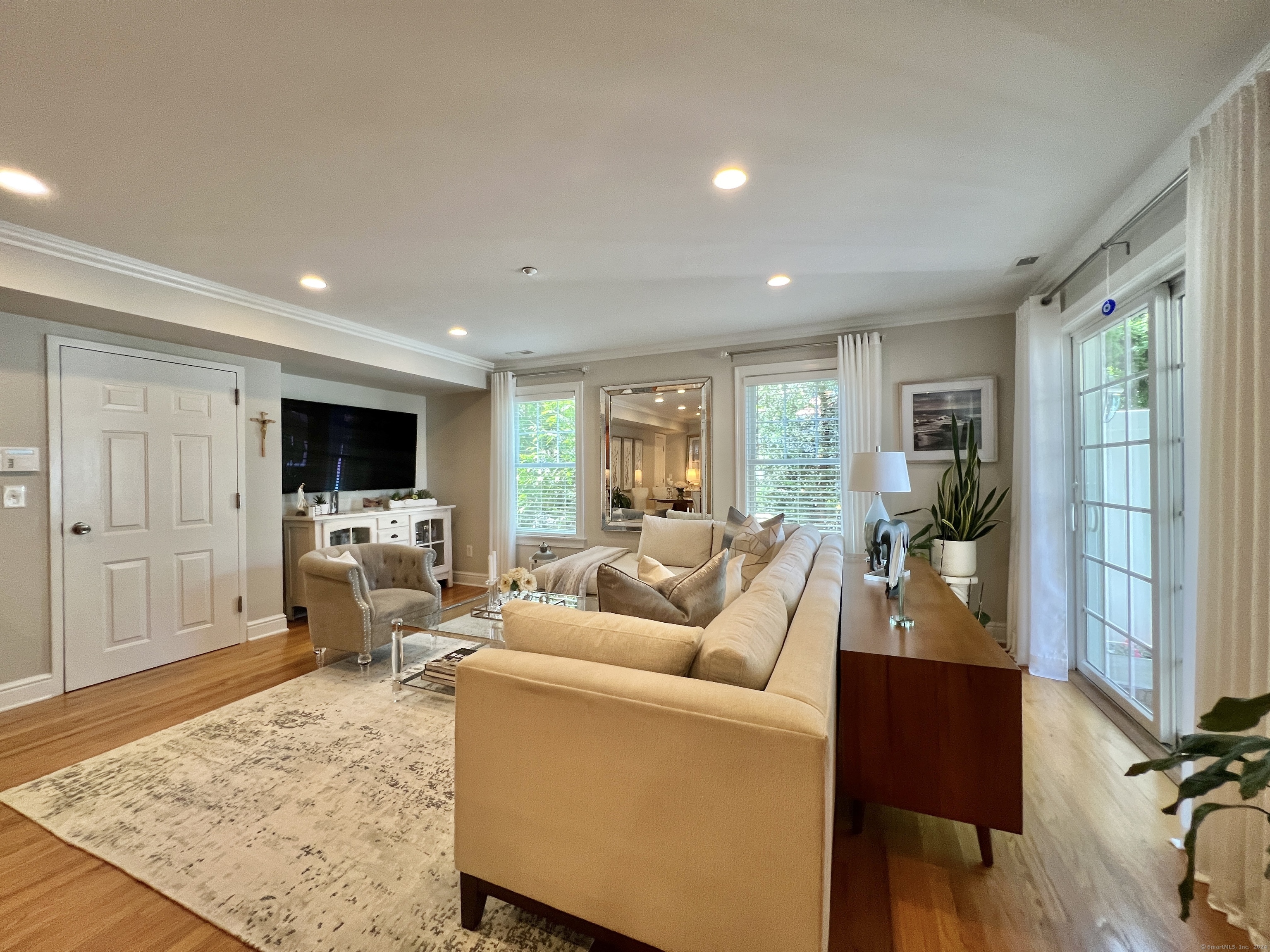 Staged living room with a beige sectional, tufted armchair, hardwood floors, and glass French doors.