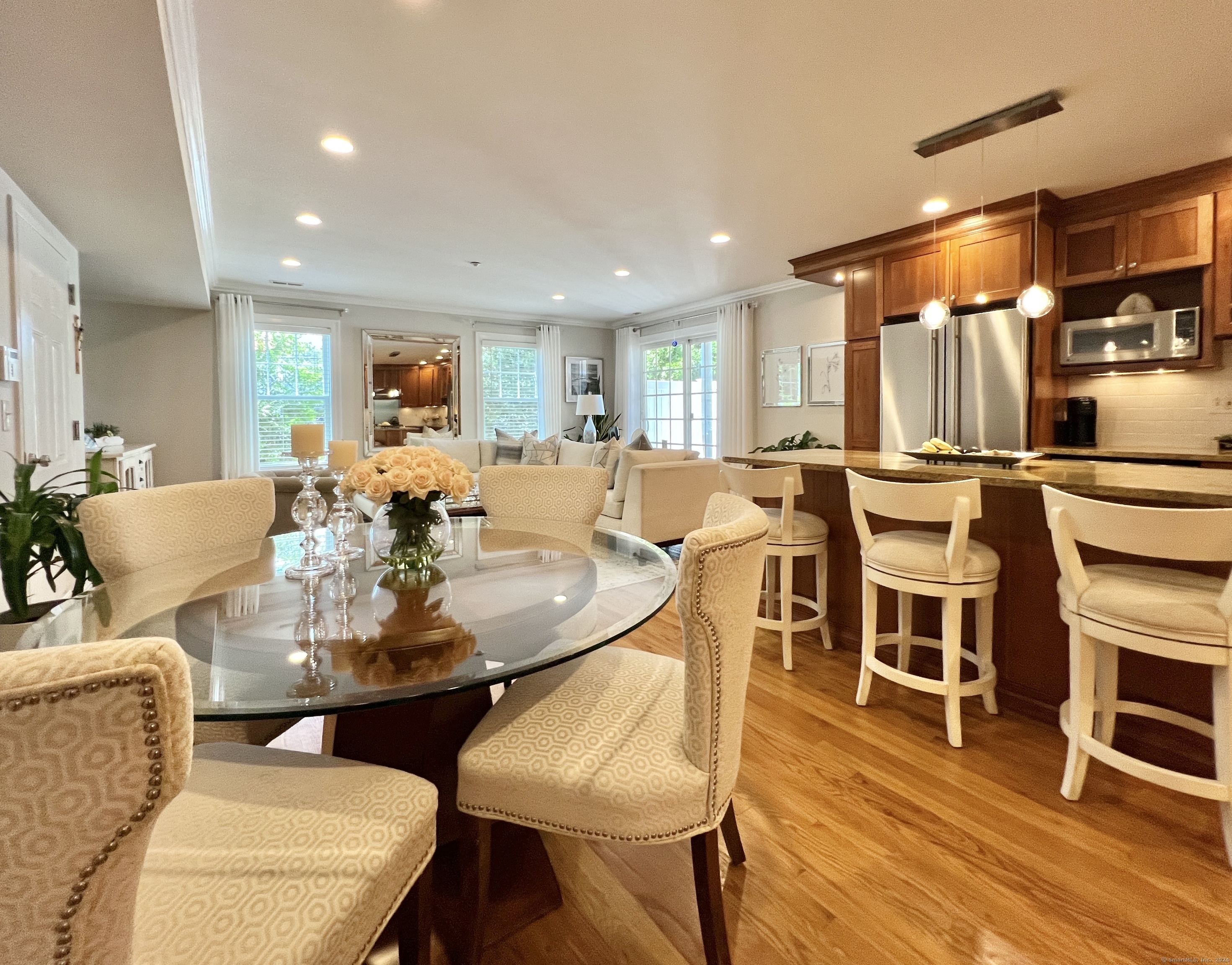 Open dining area and kitchen with a glass table, cream chairs, and a dark-wood island with bar seating.