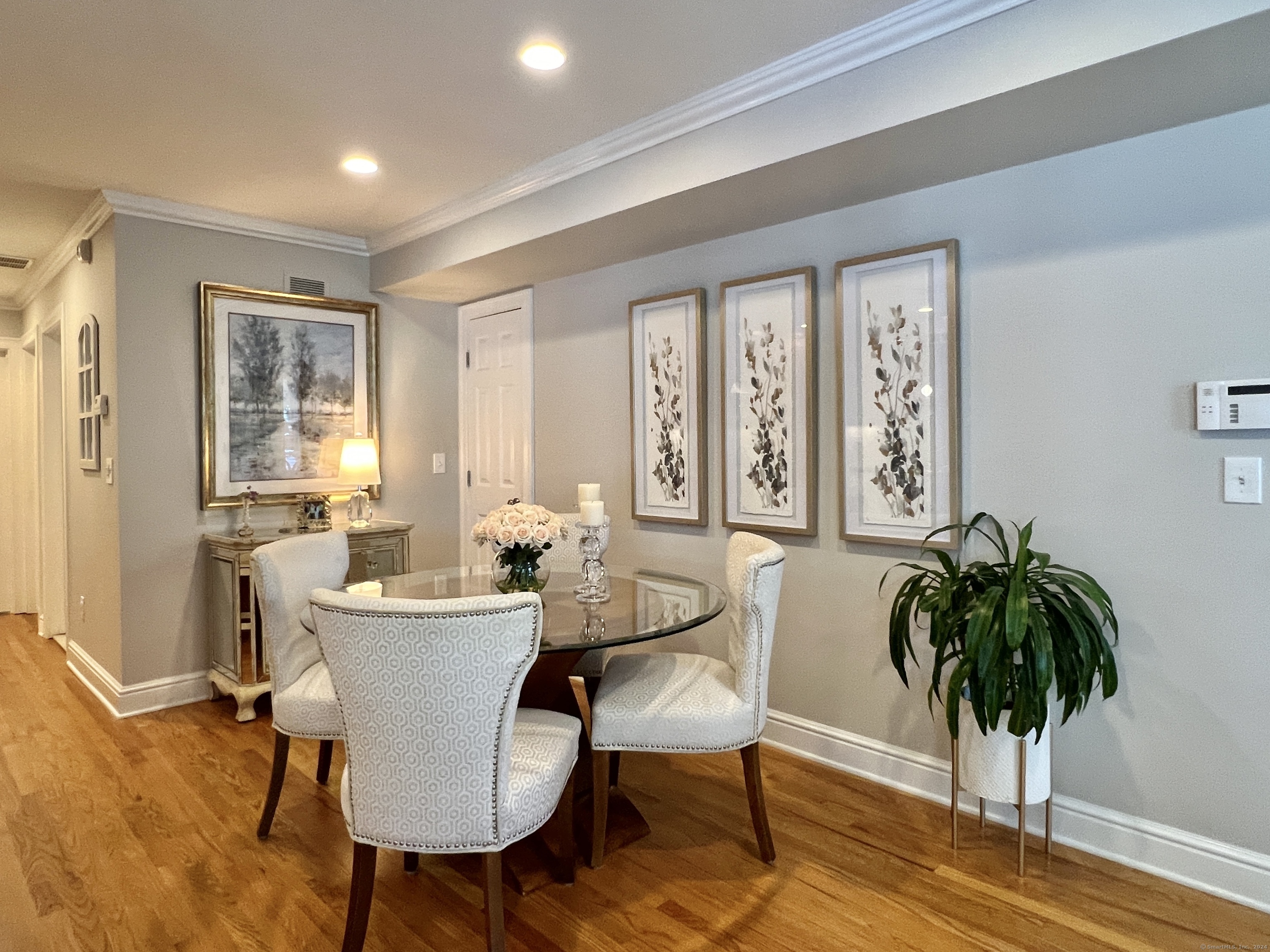 Dining area with a glass-top table, upholstered chairs, and framed botanical prints.