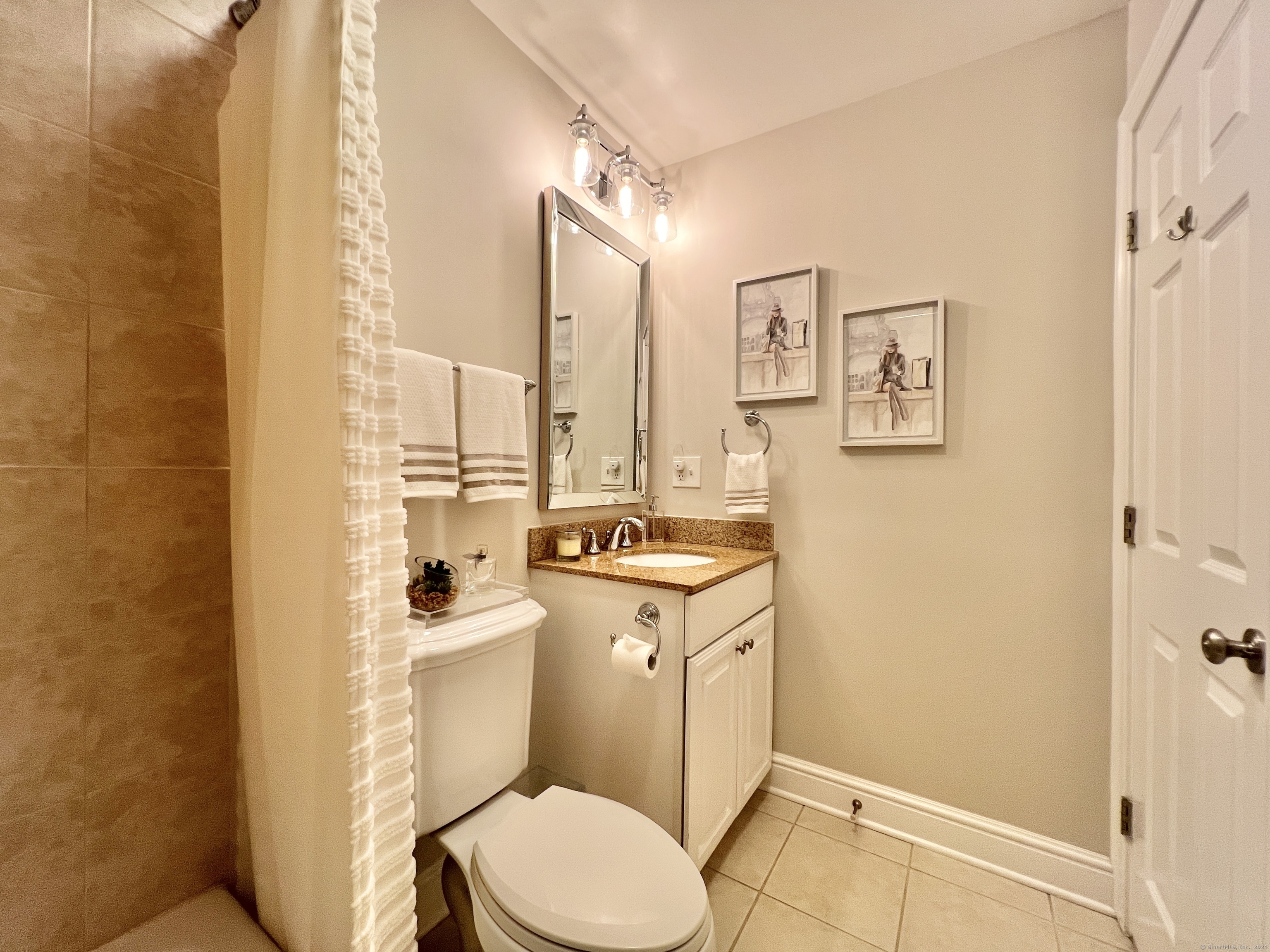 Bathroom with a tiled shower, white toilet, and granite-topped vanity.