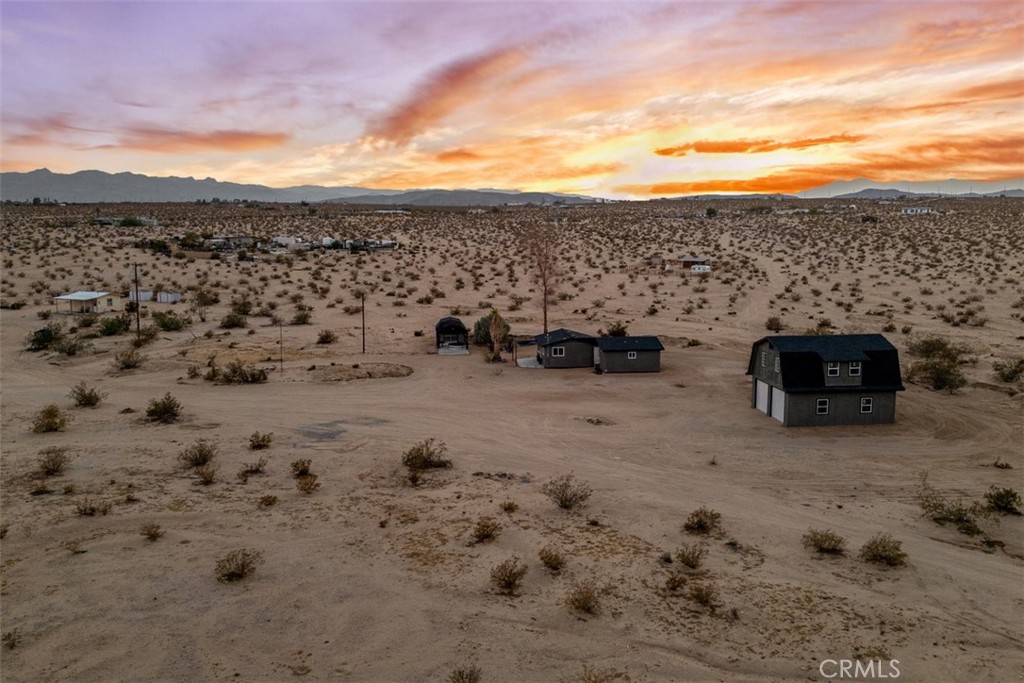 Aerial view of desert property with scattered homes and distant mountains at sunset.