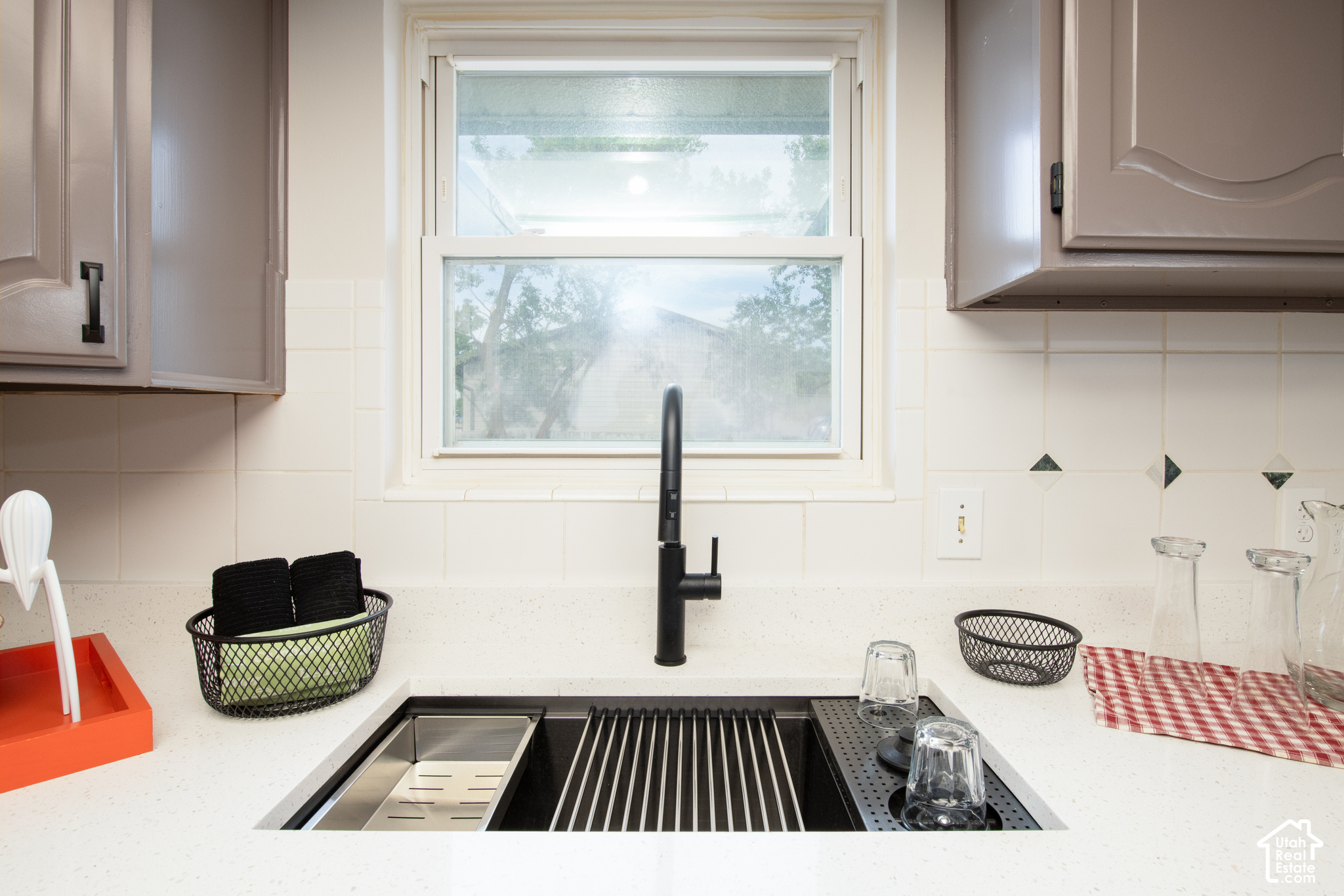 Kitchen sink with a black faucet, stainless steel drying rack, and window above the counter.