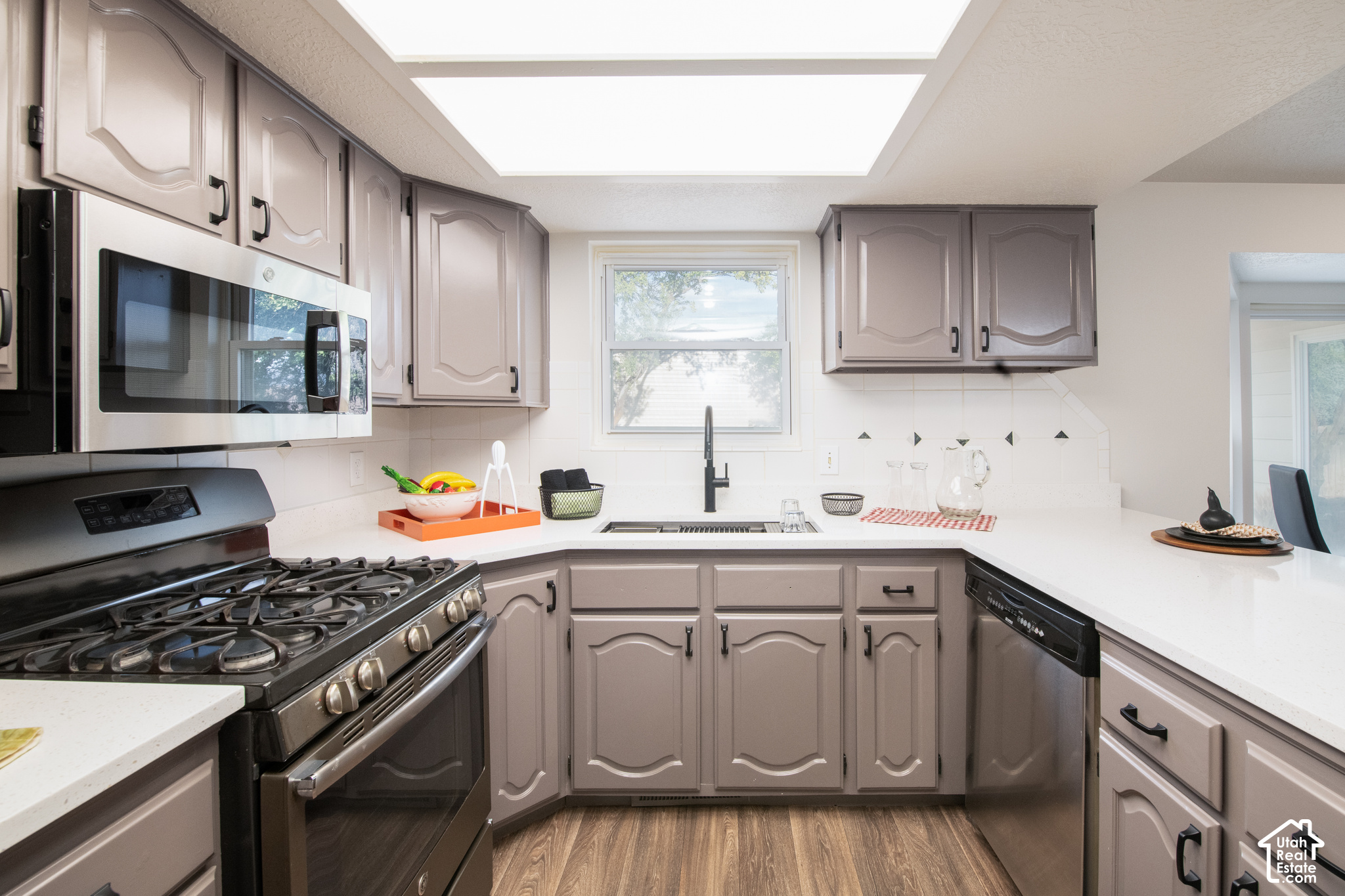 Kitchen with taupe cabinets, white counters, stainless appliances, and a gas range.