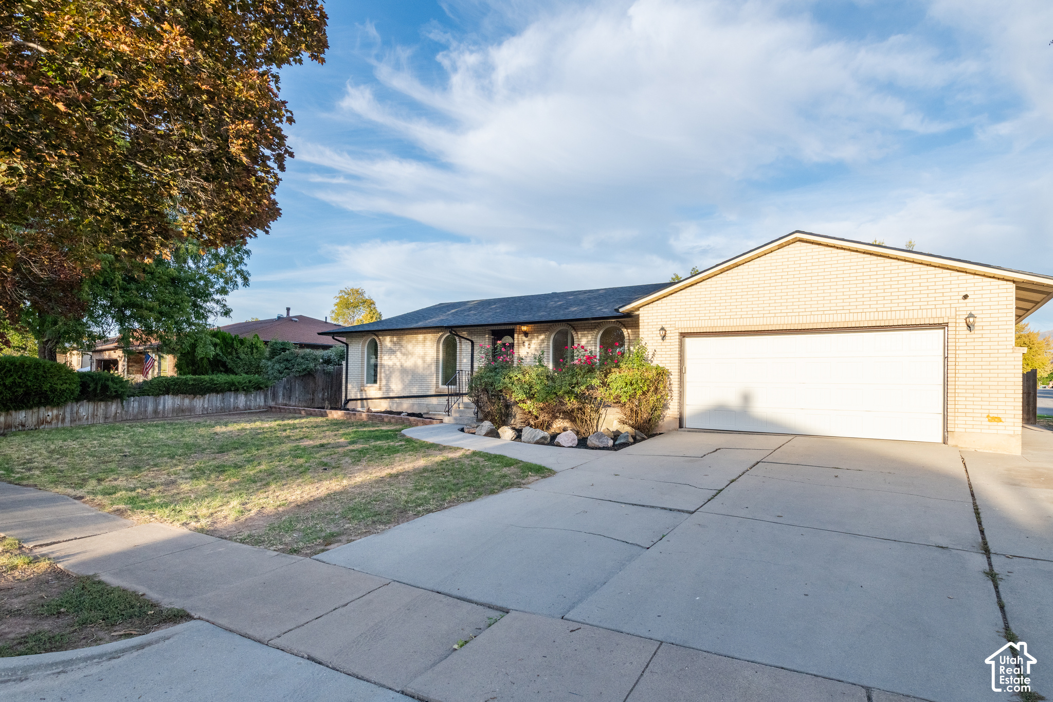 Light brick home with arched windows, a white double garage door, and a broad concrete driveway.