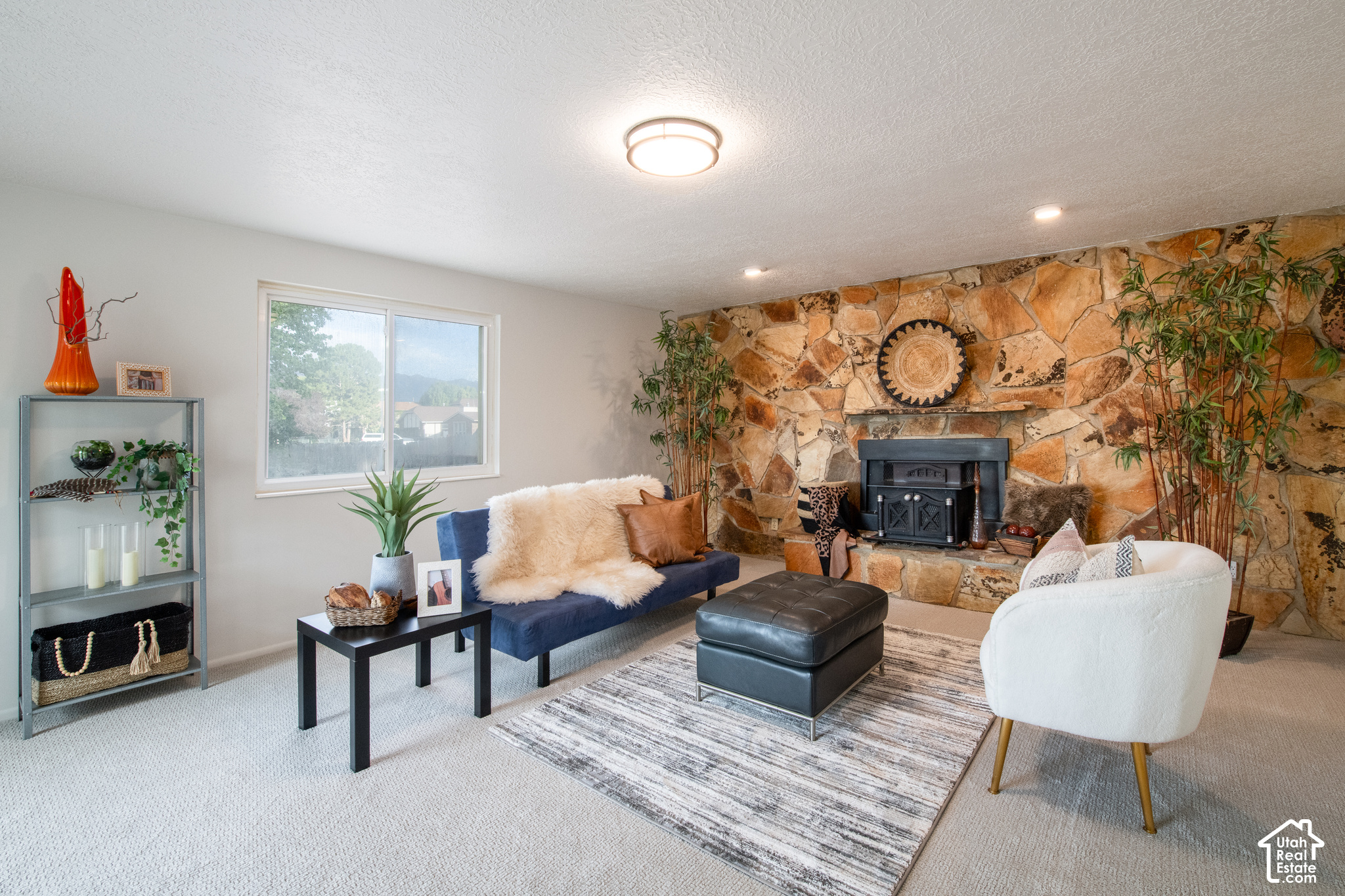 Living room with a stone fireplace, blue sofa, white armchair, and large window.